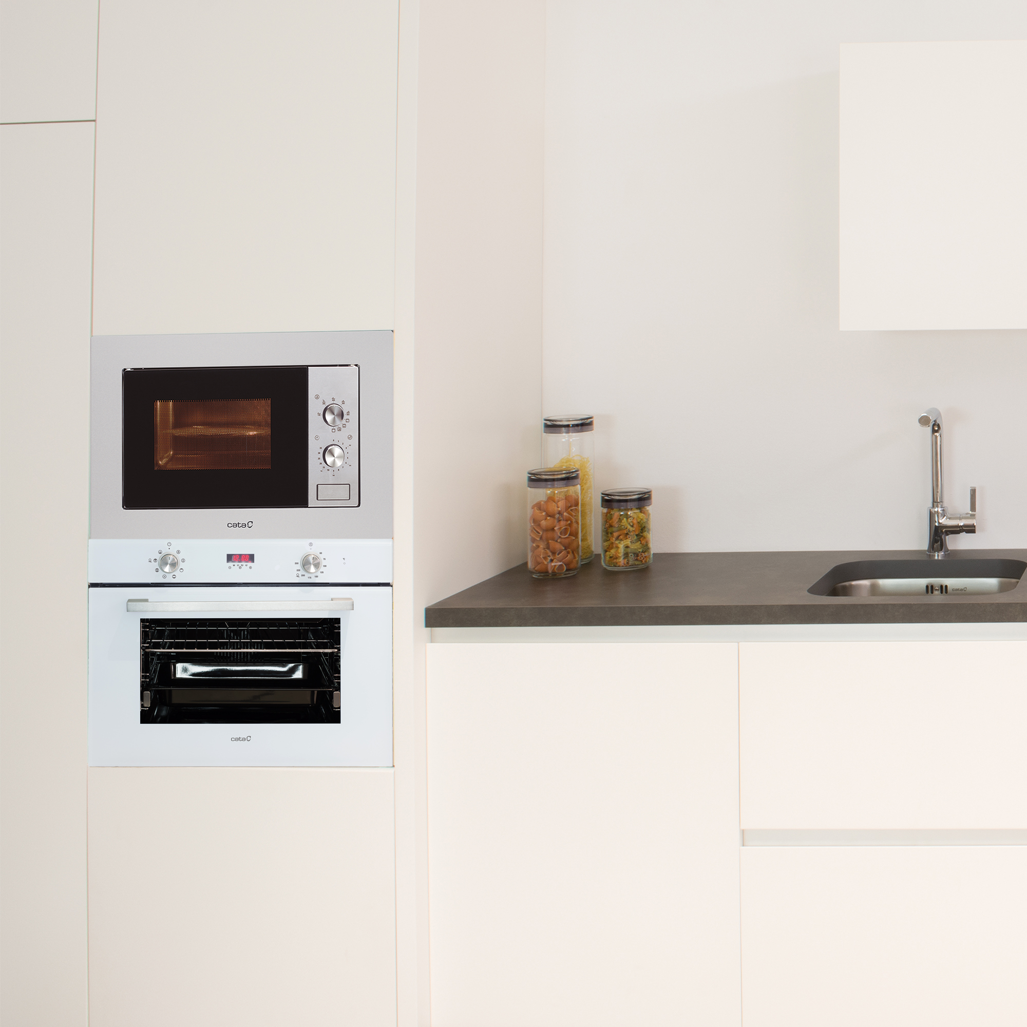 Cocina con horno y microondas empotrados, botes con comida en la encimera. Armarios beige.