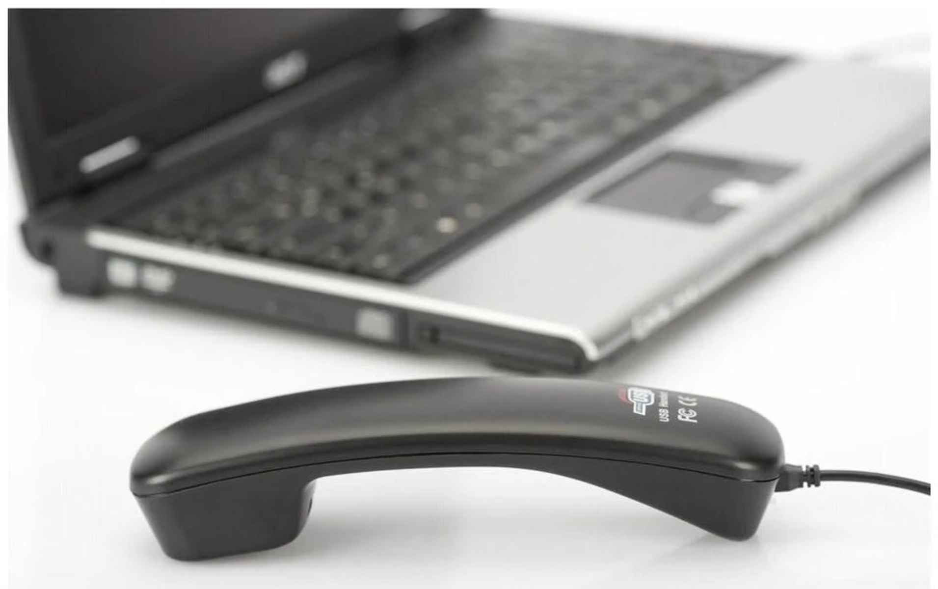 Schwarzes Telefon-Headset mit Laptop im Hintergrund. Das Headset liegt auf weißer Oberfläche.