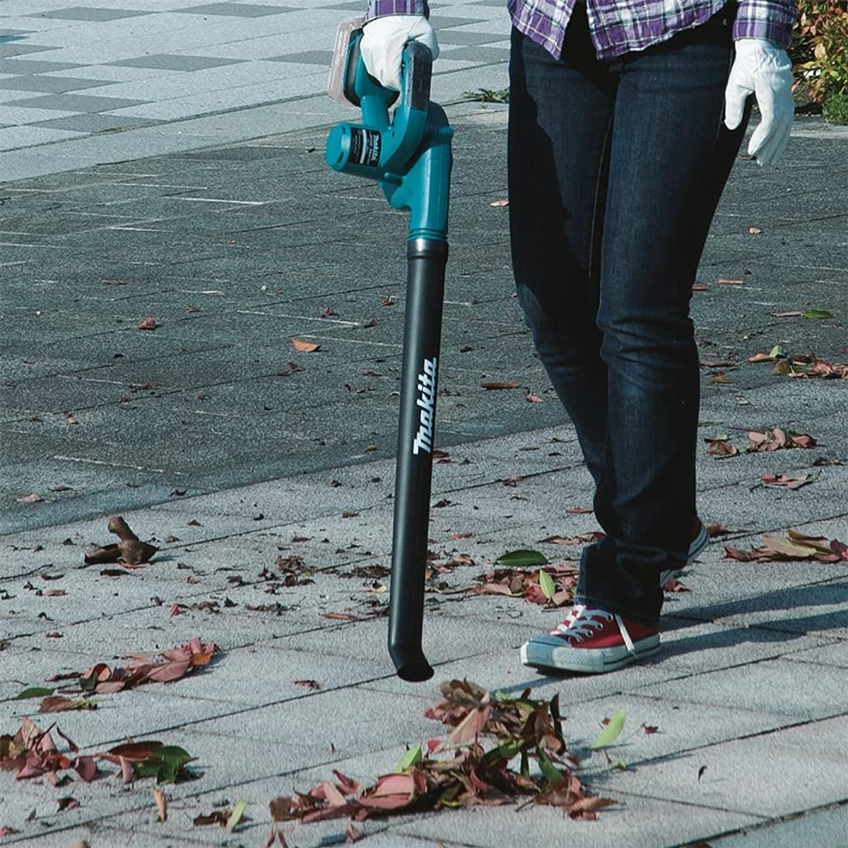 A person using a leaf blower on a stone path. Leaves are being blown away. The person wears red shoes.