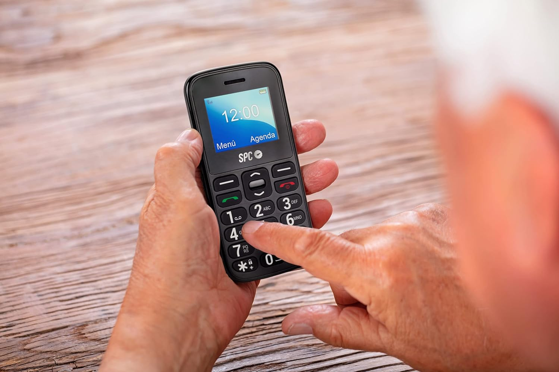 Die Hände einer älteren Person halten ein einfaches schwarzes Mobiltelefon mit großen Tasten.