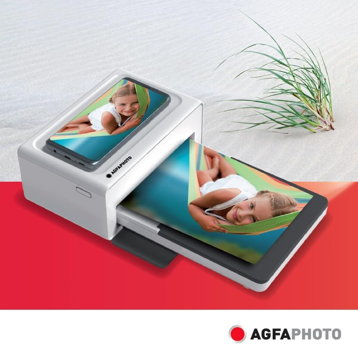 Obraz przedstawia białą drukarkę fotograficzną drukującą zdjęcie dziecka w hamaku. Drukarka ma logo AgfaPhoto.