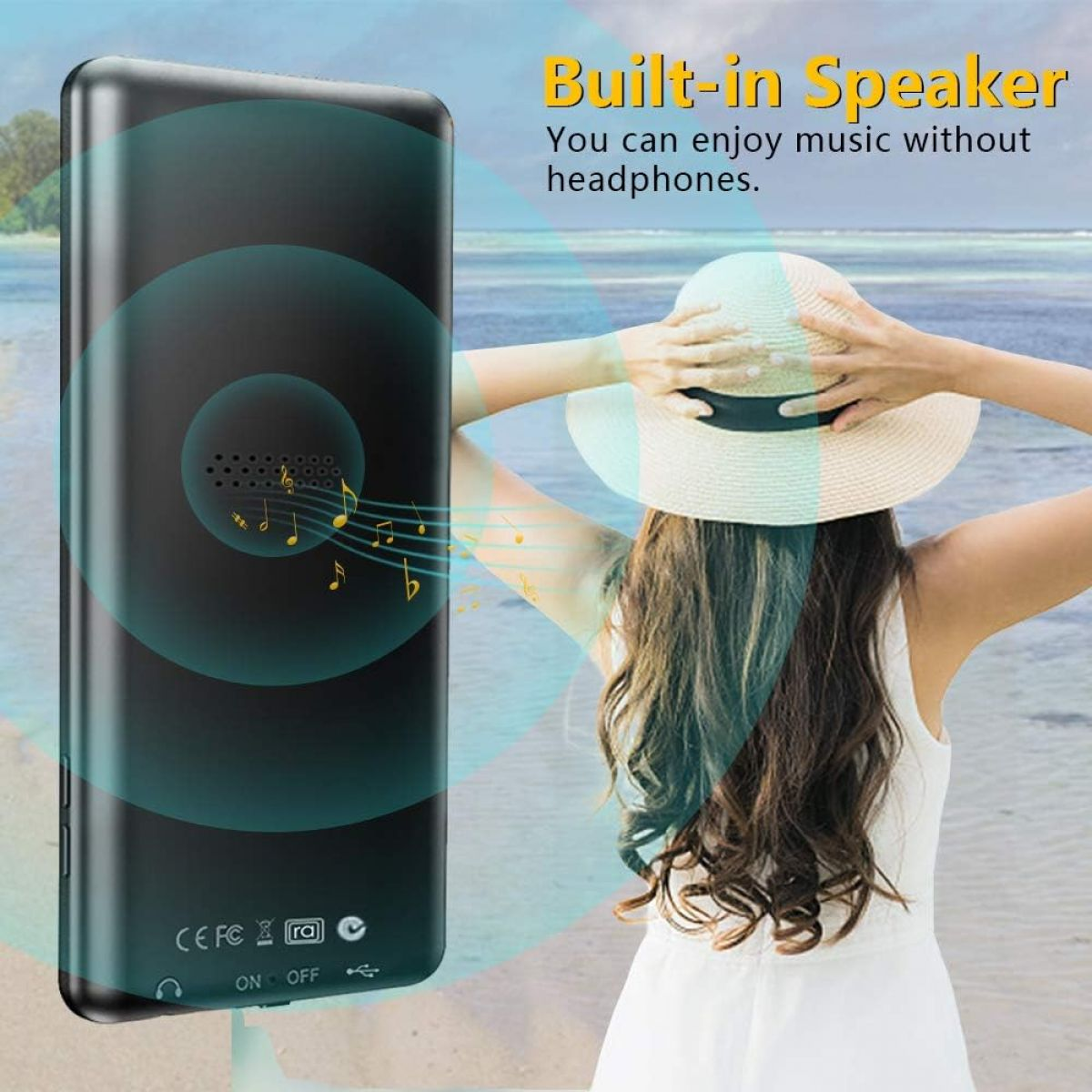 Eine Frau mit Hut hört Musik von einem schwarzen Lautsprecher am Strand.