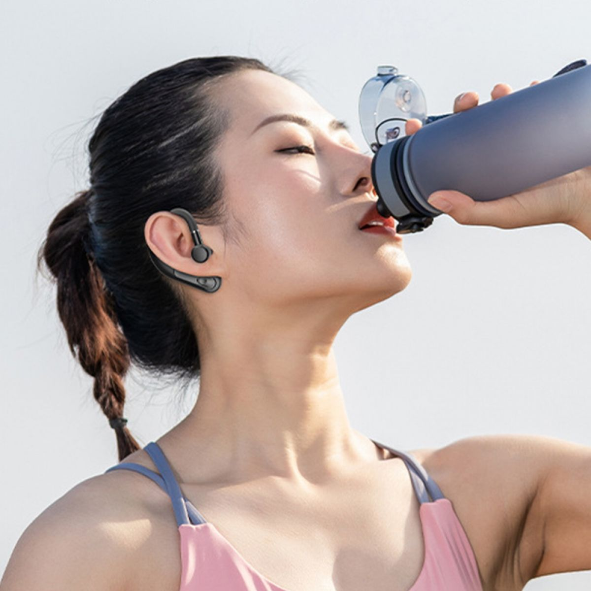 Eine Frau mit Headset trinkt Wasser aus einer Flasche im Freien mit Licht.