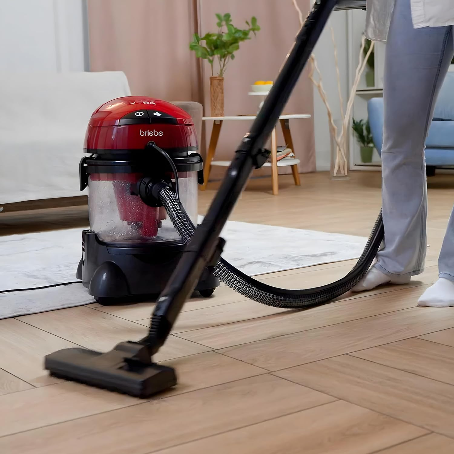 Eine Person saugt einen Holzboden mit einem rot-schwarzen Staubsauger. Der Hintergrund zeigt ein Wohnzimmer.