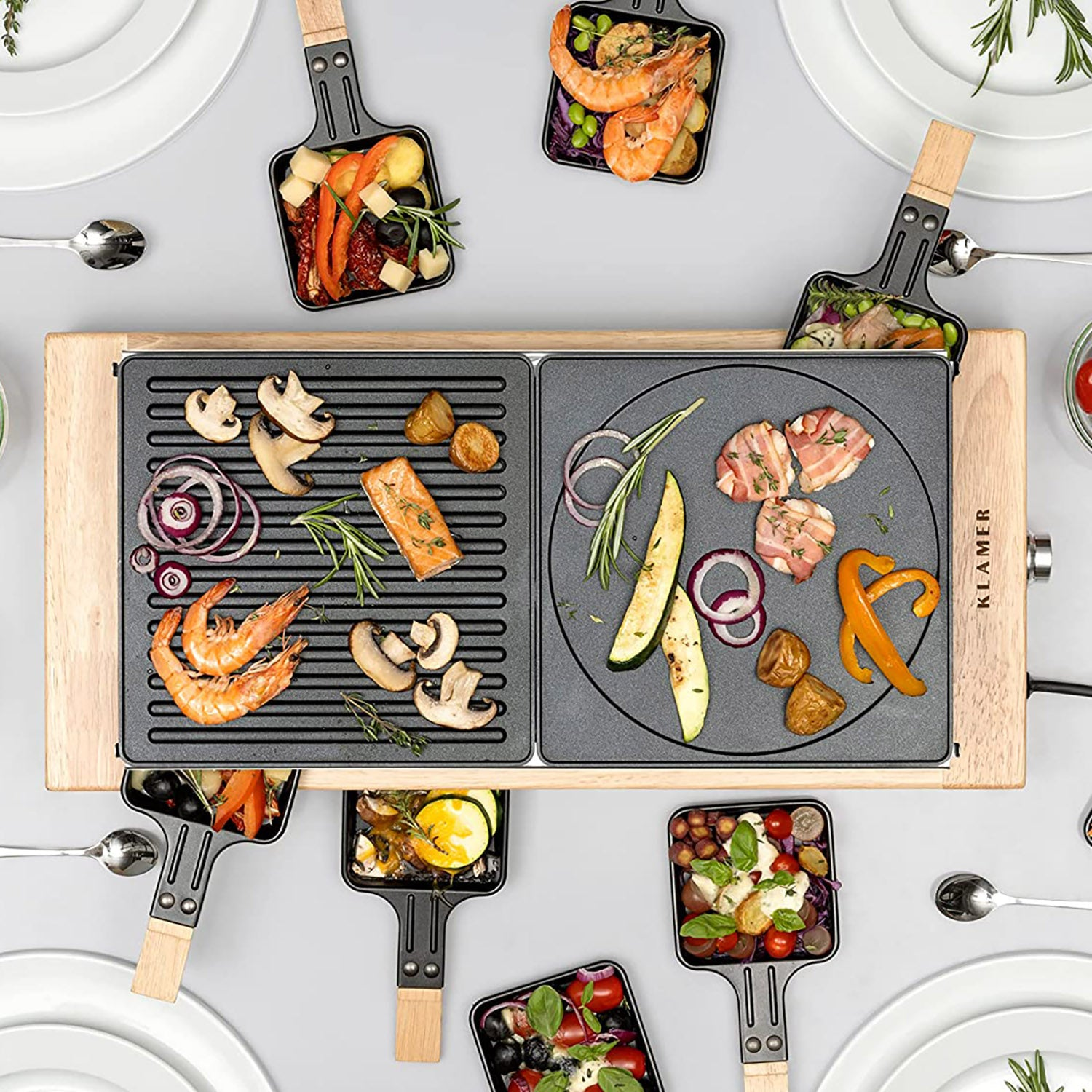 Raclette-Grill mit verschiedenen gekochten Speisen, mit Löffeln und Tellern darum herum.