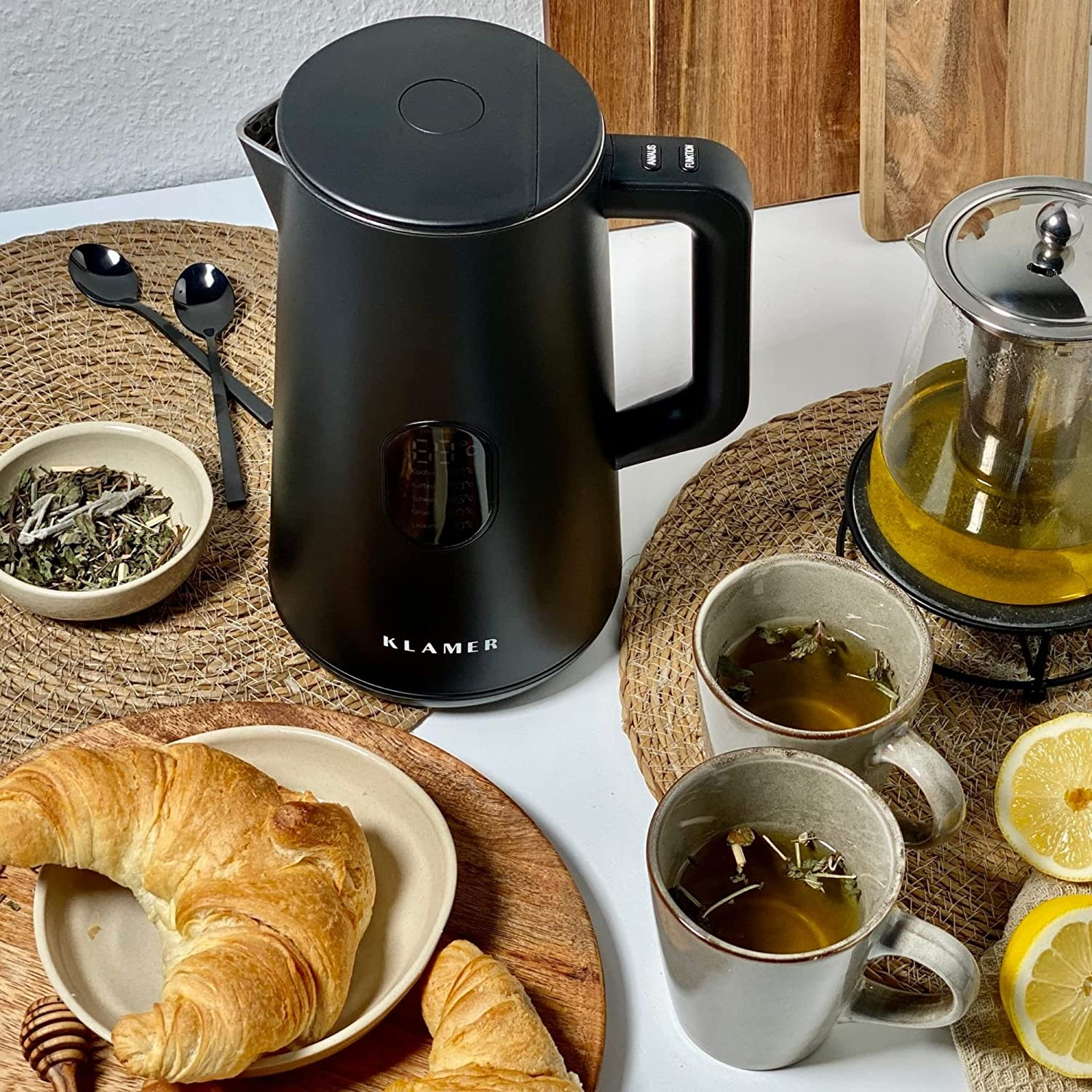 Ein schwarzer Wasserkocher mit Tassen, Croissant und Teezutaten.