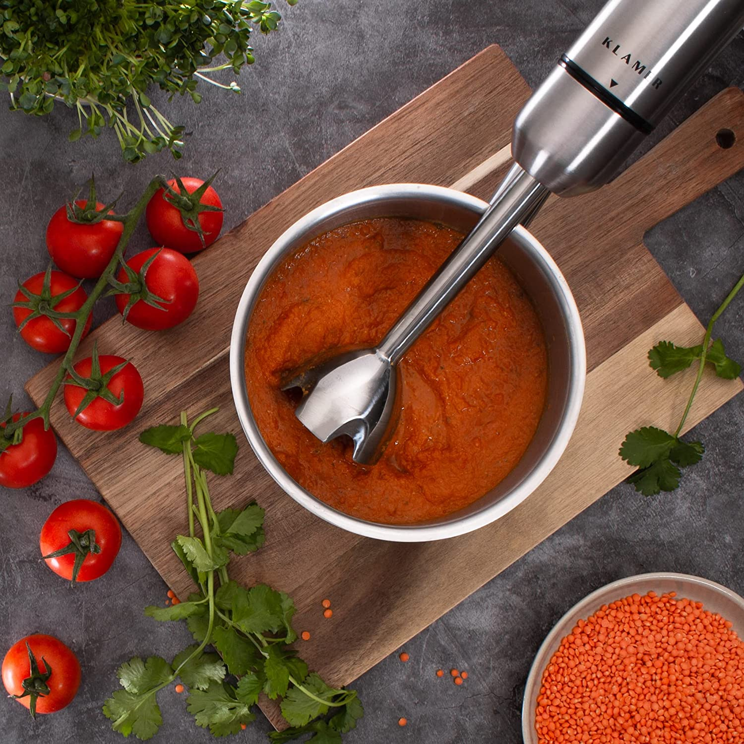 Tomaten, eine Schüssel mit Soße und ein Mixer auf einem Holzbrett. Rot und braun.