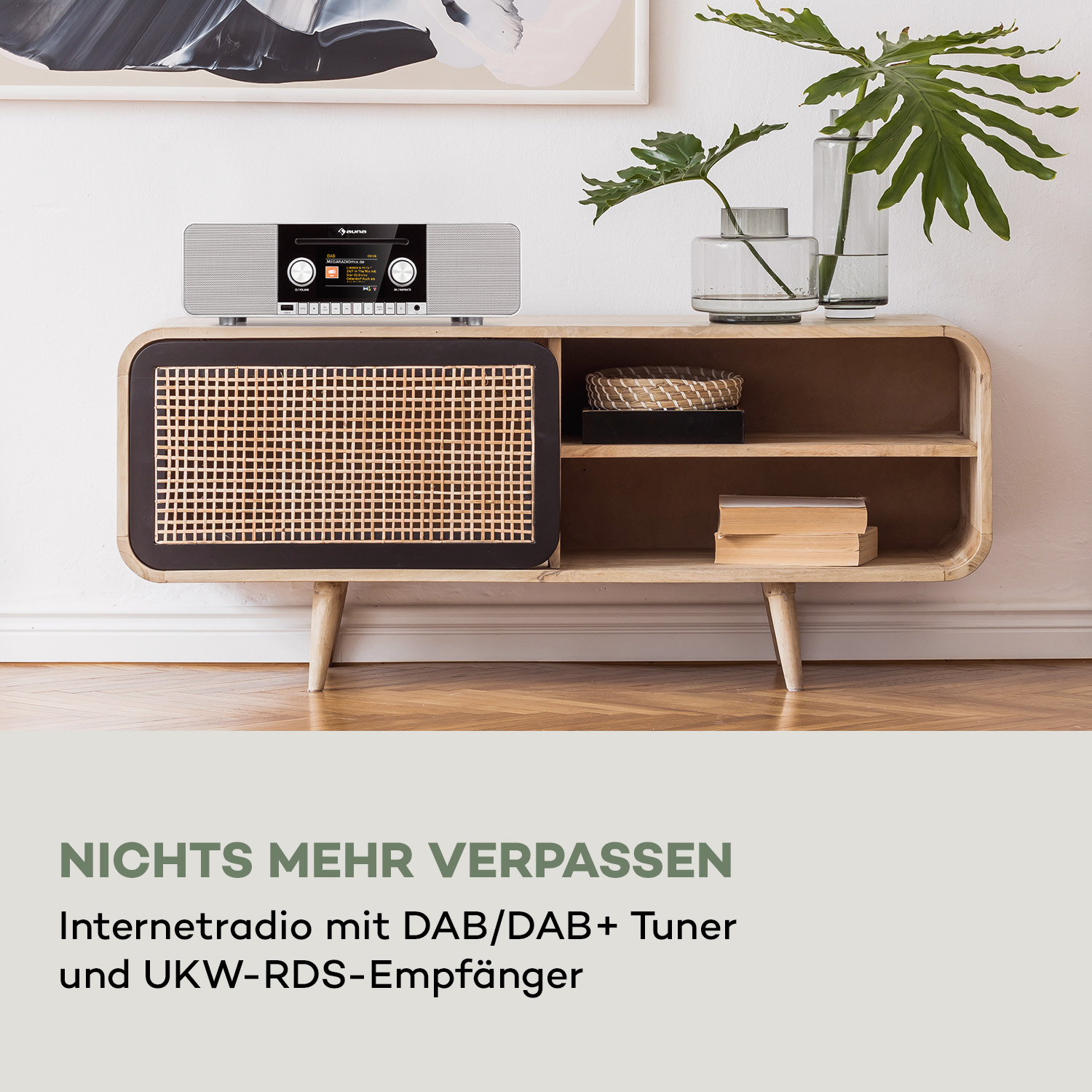 Ein weißes und silbernes Stereoanlage auf einem Holzschrank mit Pflanzen. Bücher und ein geflochtener Korb sind vorhanden.