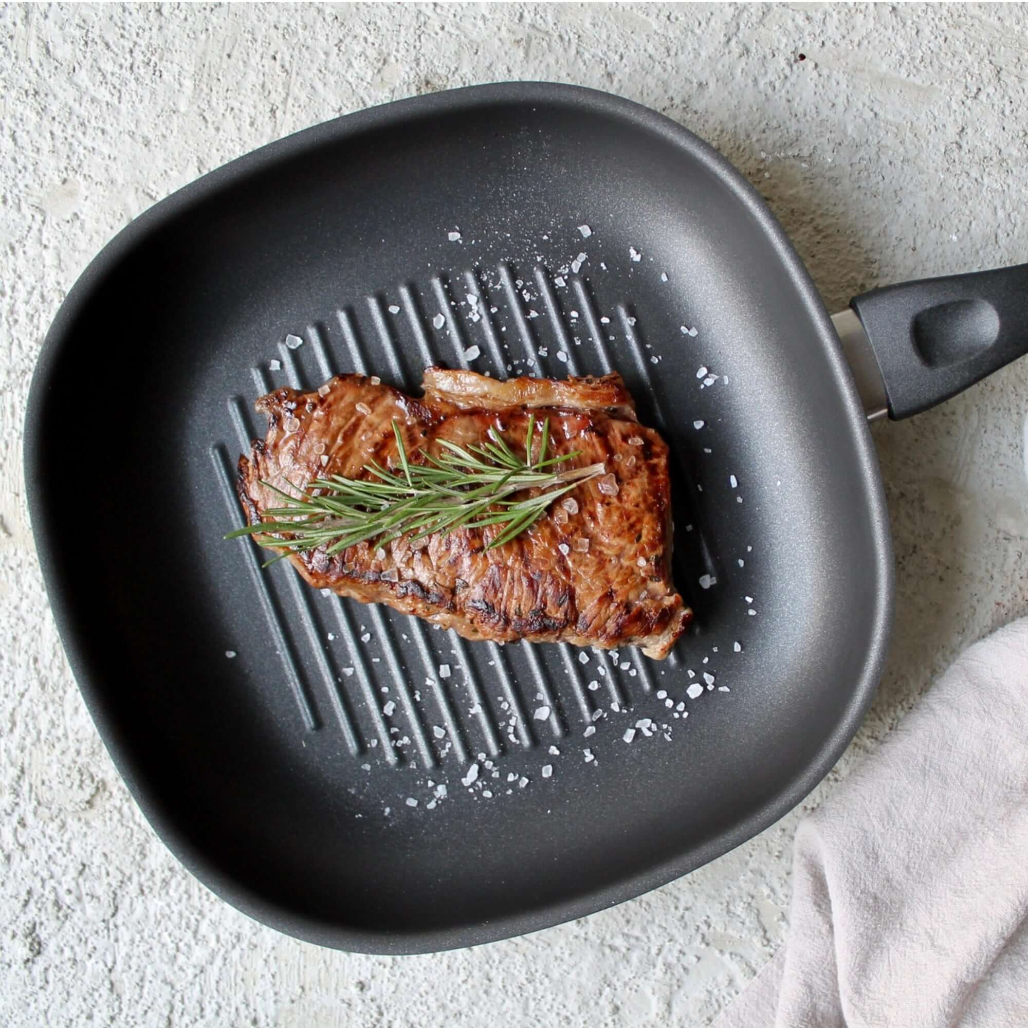 Gegrilltes Steak in einer schwarzen Pfanne. Rosmarinzweig, Salz gestreut. Hellgrauer Hintergrund.