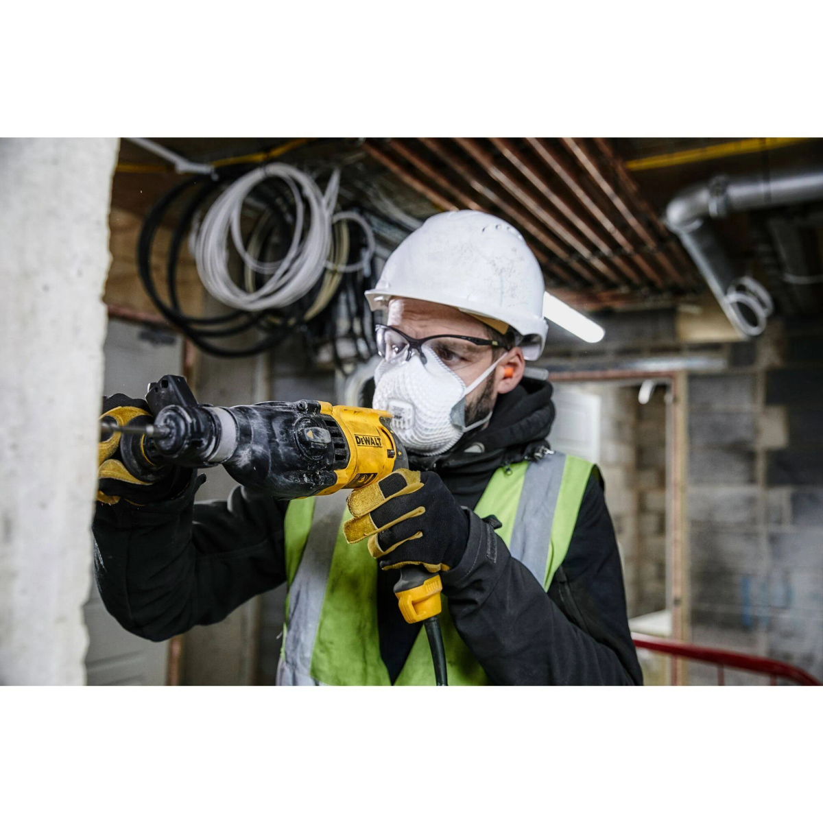 Robotnik budowlany z wiertarką, w odzieży ochronnej. Praca w budynku.