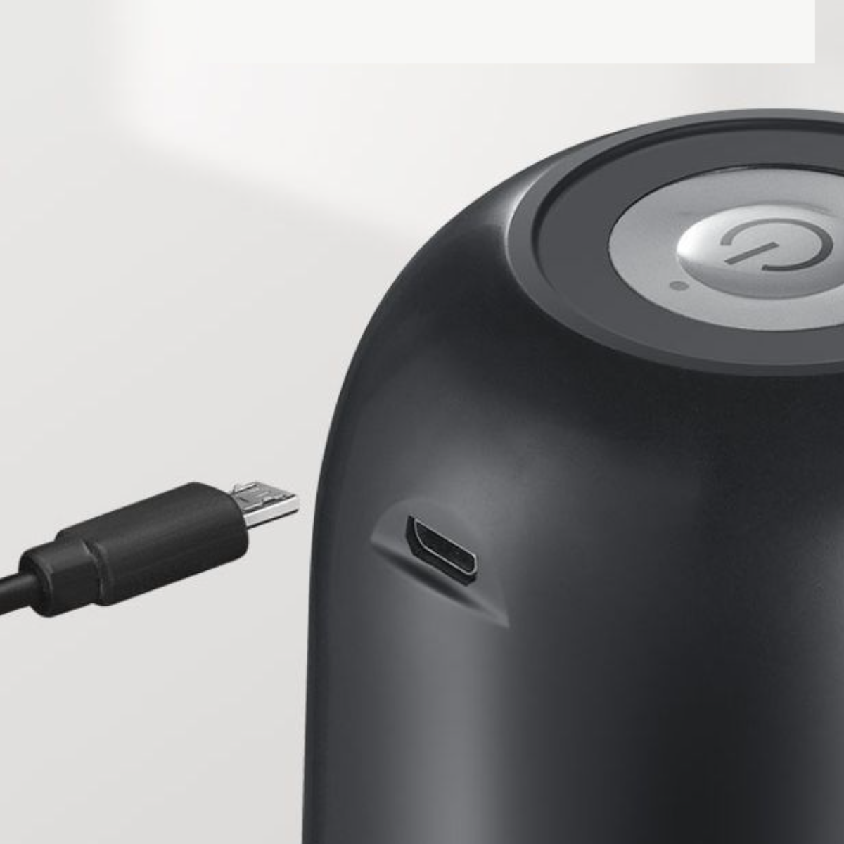 Ein schwarzes Gerät mit Ladeanschluss und Einschaltknopf. Ein USB-Kabel ist eingesteckt.