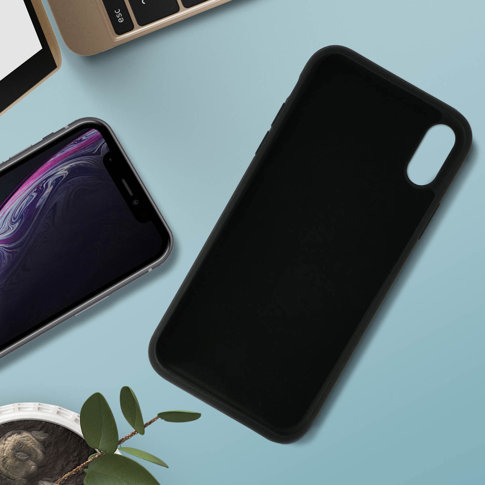 Een telefoon met een zwarte hoes ligt naast een andere telefoon. Er is een groene plant. De achtergrond is blauw.