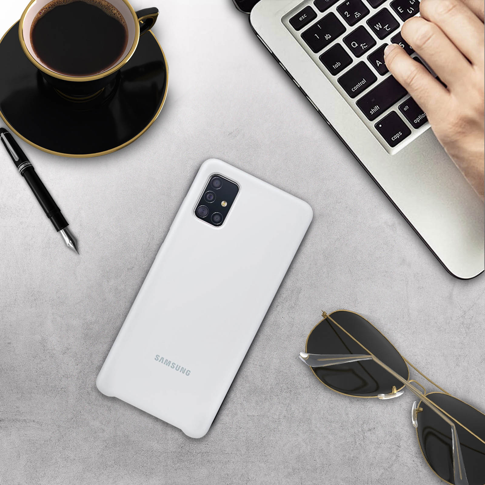 Draufsicht auf einen Schreibtisch mit Telefon, Laptop, Stift, Sonnenbrille und einer Tasse Kaffee.