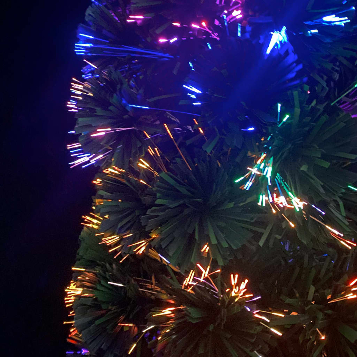 Nahaufnahme eines Glasfaser-Weihnachtsbaums mit bunten Lichtern. Dunkler Hintergrund.