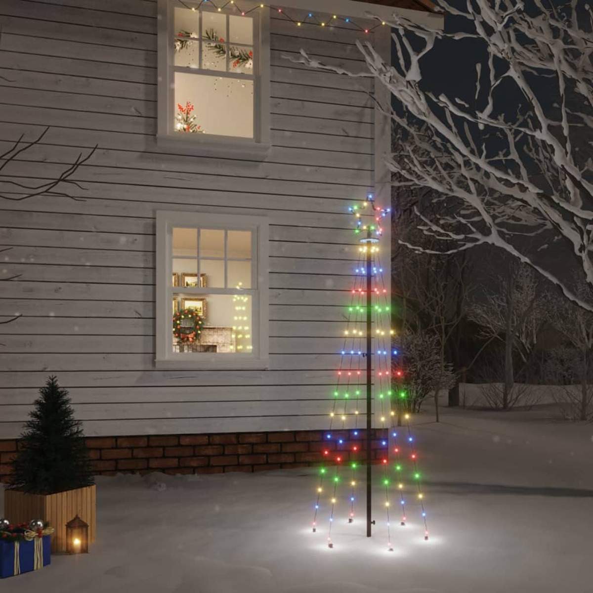 Weihnachtsbaum im Freien mit bunten Lichtern. Schneebedeckter Boden, Haus im Hintergrund.