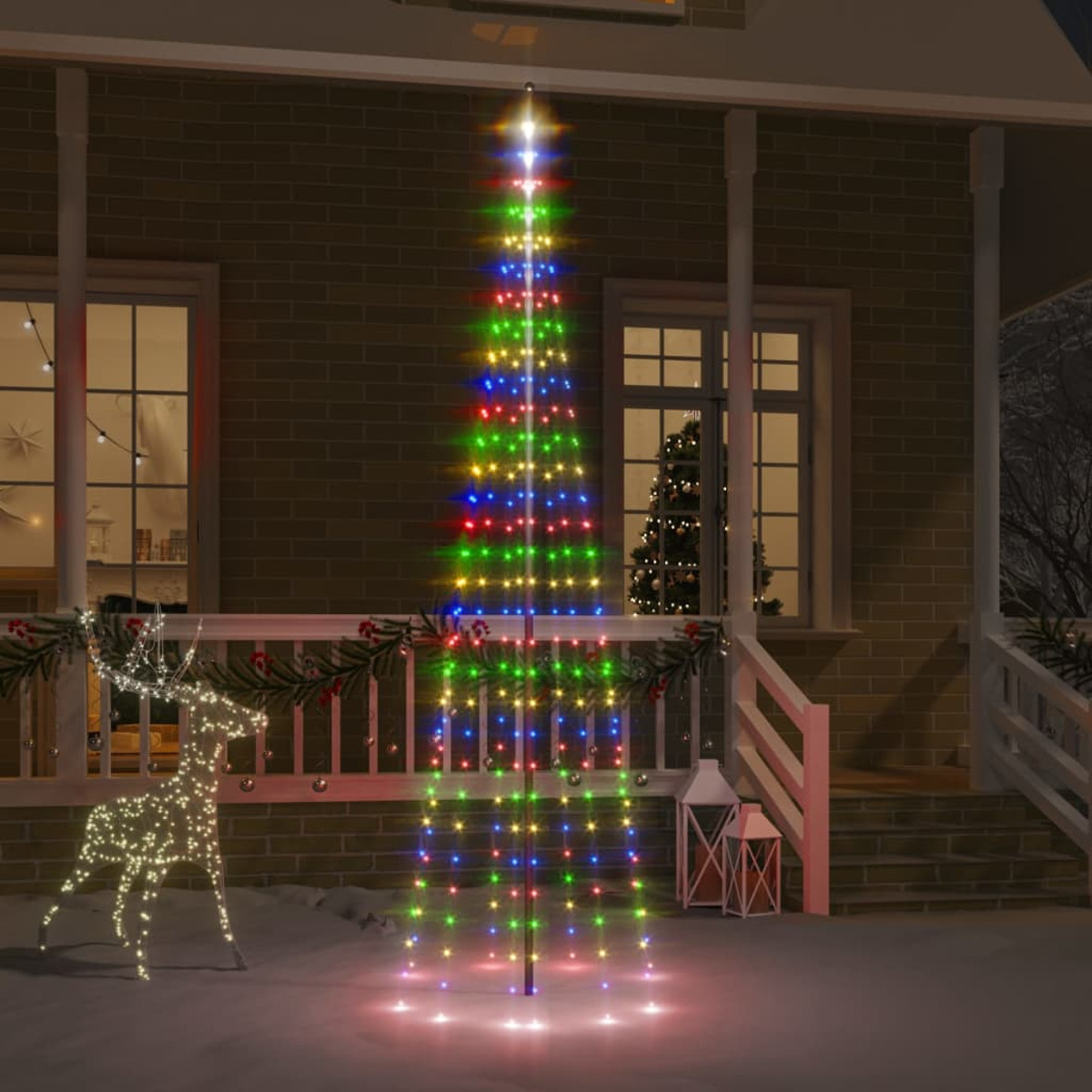 Ein Haus ist mit Weihnachtsbeleuchtung, einem beleuchteten Baum, einer Rentierfigur und Schnee dekoriert.