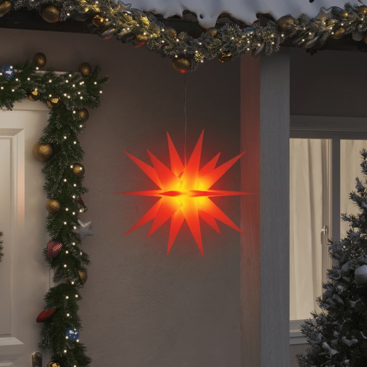 Rote sternförmige Weihnachtsdekoration, die vor einem Haus hängt, mit Girlande und Schnee.