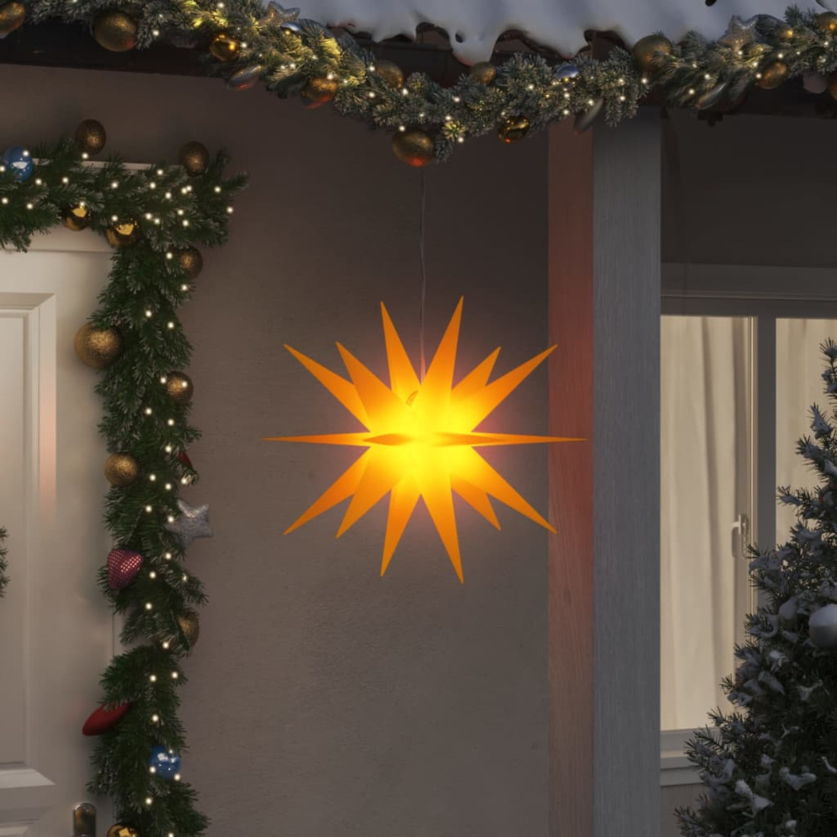 Eine gelbe sternförmige Weihnachtsdekoration hängt draußen an einem Haus, andere Dekorationen sind sichtbar.