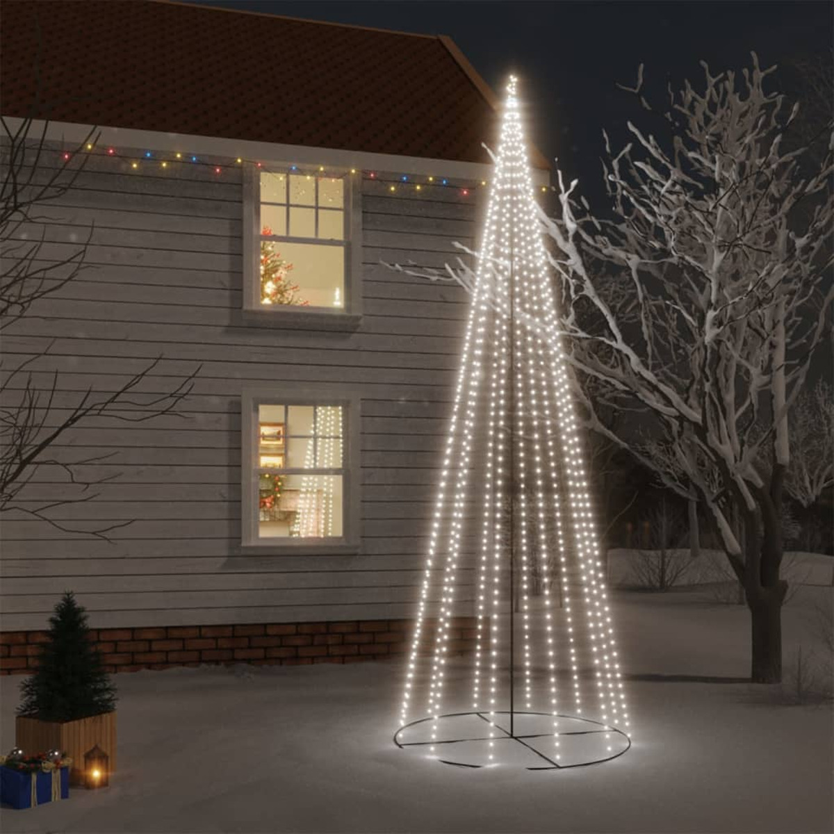 Eine beleuchtete Weihnachtsbaum-förmige Anzeige vor einem Haus bei Nacht, umgeben von Schnee.