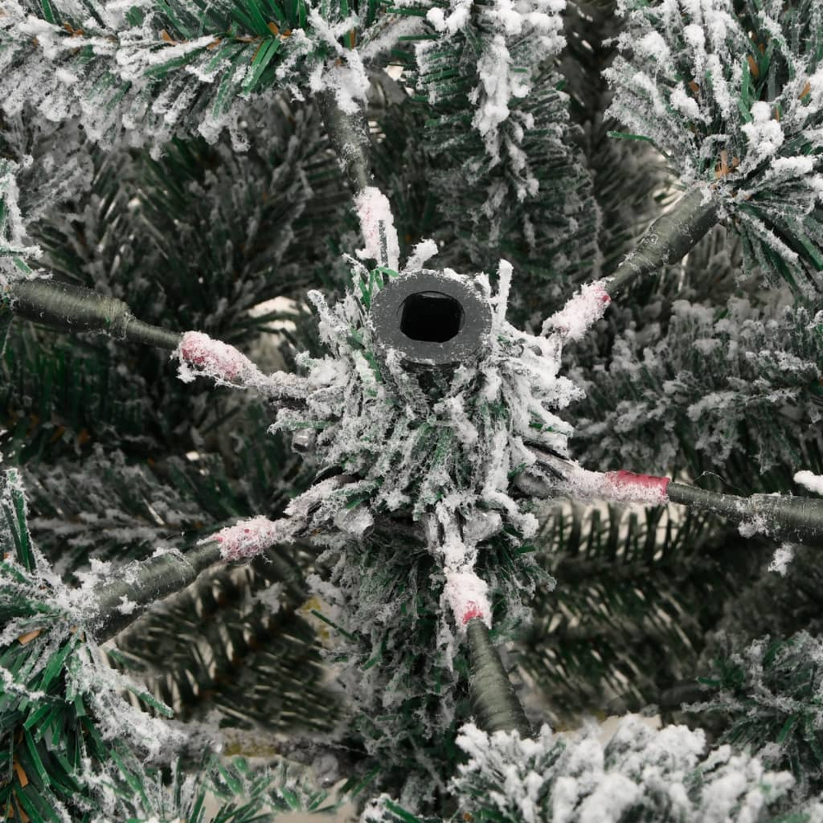 Nahaufnahme eines schneebedeckten Weihnachtsbaumfußes und -ästen mit grünen Nadeln.