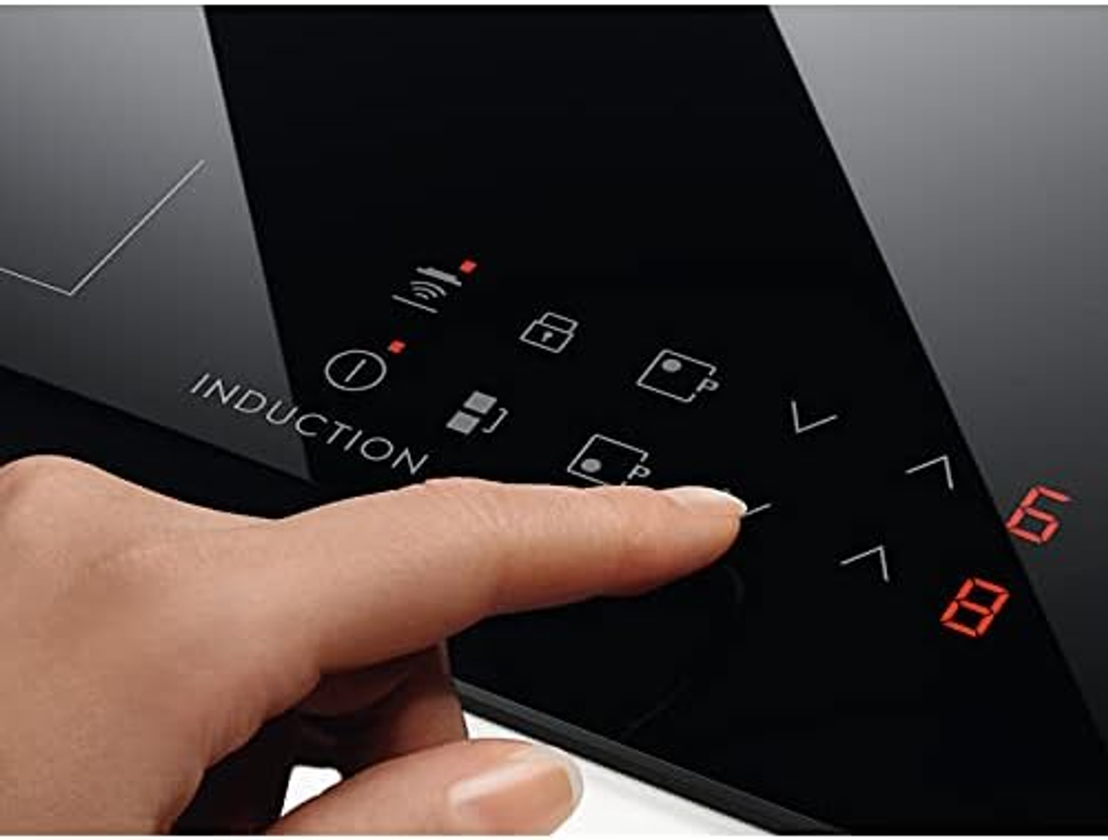 Zbliżenie palca naciskającego przycisk na czarnej płycie indukcyjnej.