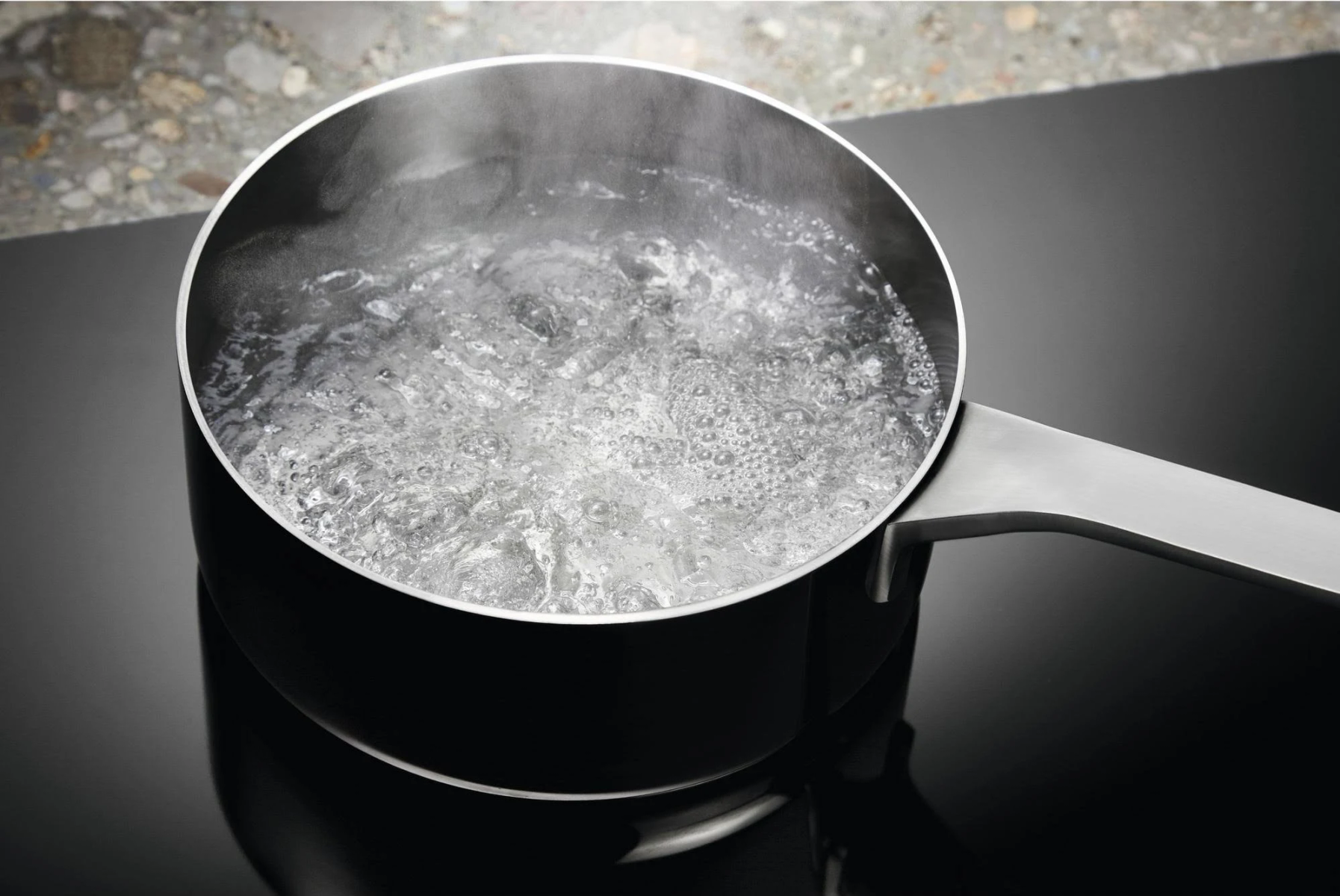 Czarny garnek z wrzącą wodą na czarnej płycie kuchennej, para unosi się z wody.