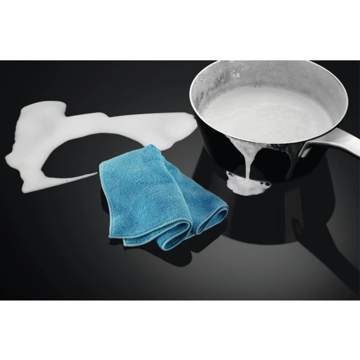 Niebieska ściereczka do czyszczenia obok garnka z pieniącym się płynem na czarnej płycie kuchennej, widoczne rozlanie.