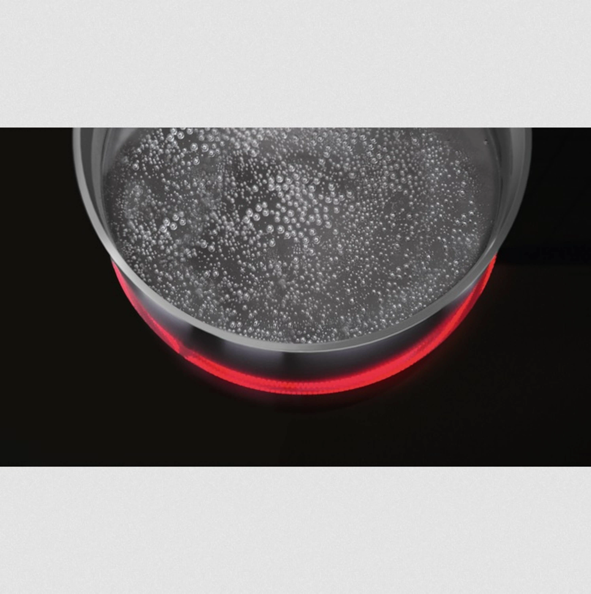 Een doorzichtige glazen pot met kokend water op een rode inductiekookplaat. Bubbels zijn zichtbaar.