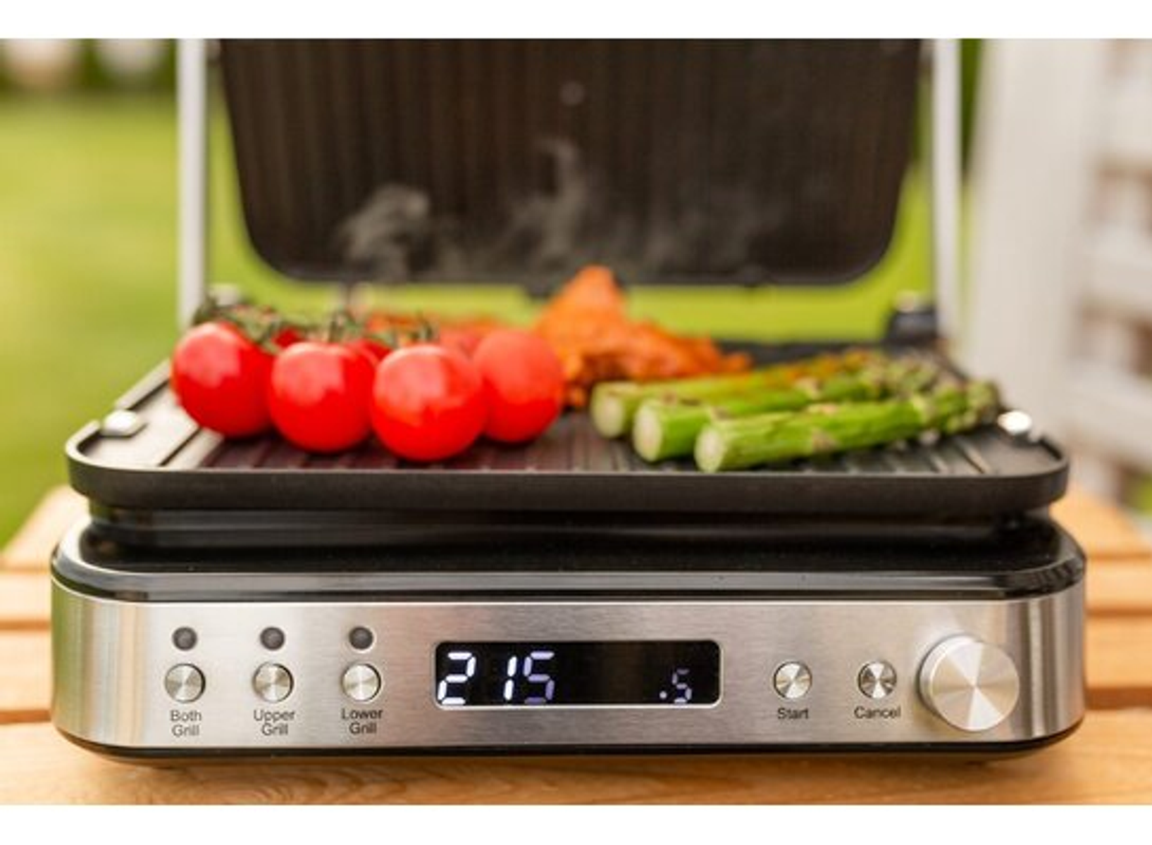 Ein offener Grill mit Tomaten und Spargel. Digitalanzeige zeigt 215 Grad. Umgebung im Freien.
