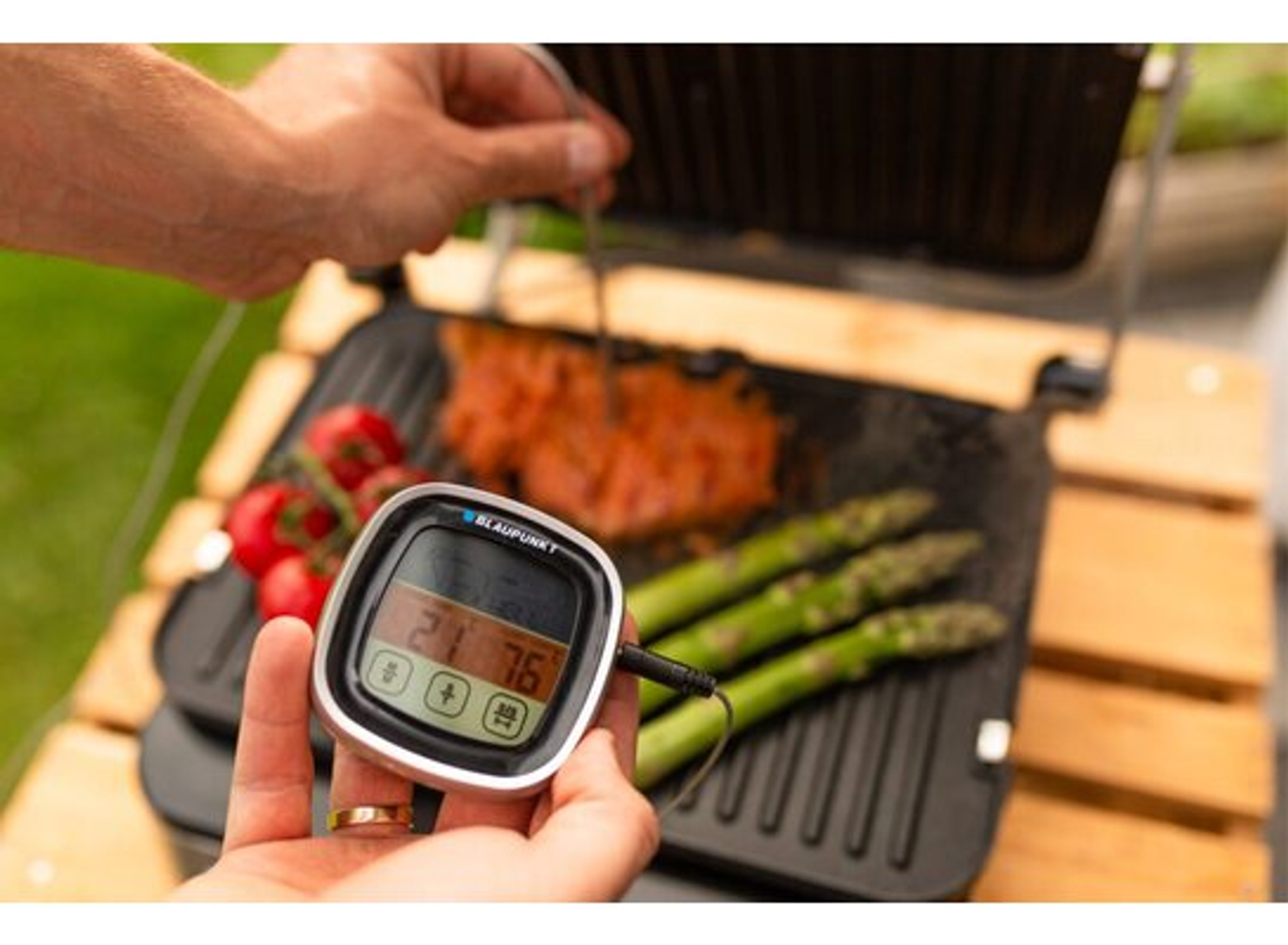 Hand, die ein digitales Fleischthermometer über einer Panini-Presse mit Steak und Spargel hält.