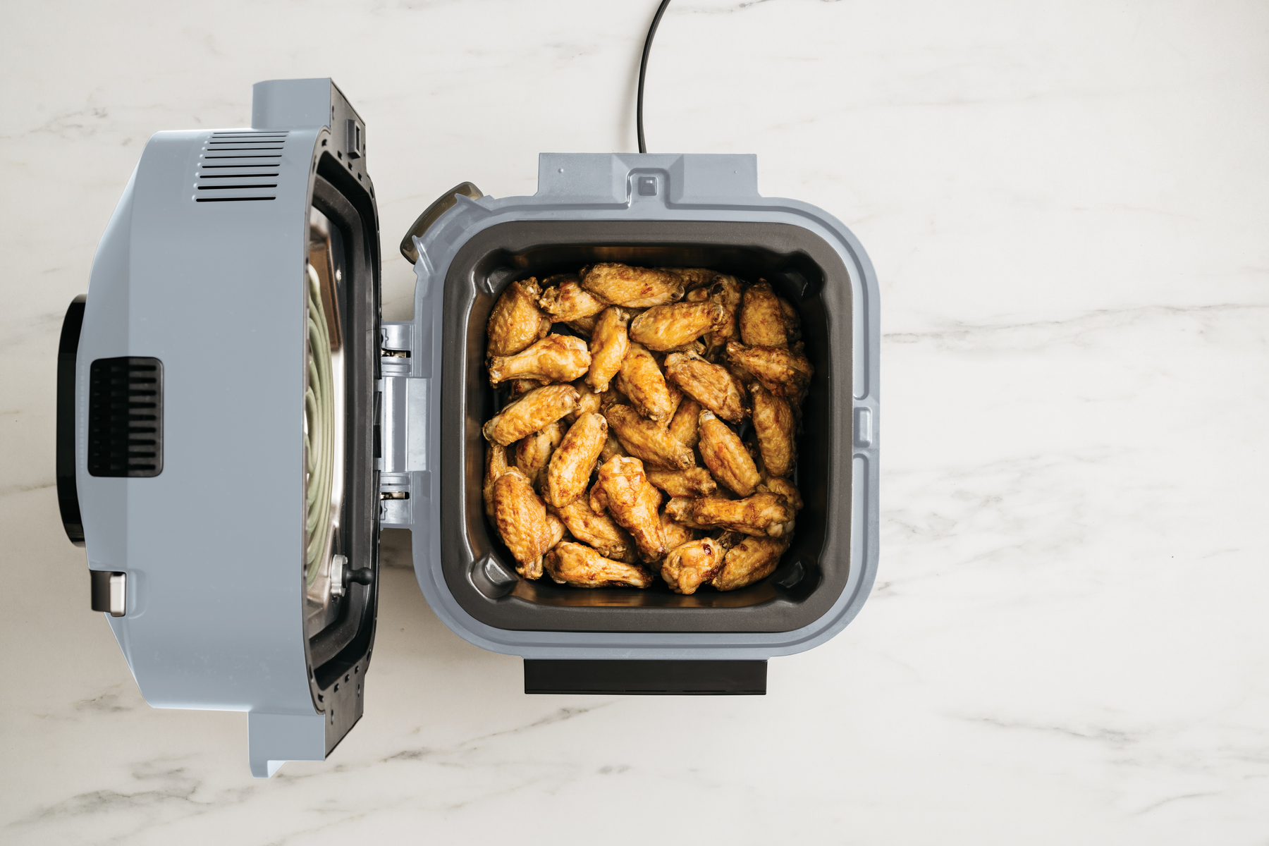 Air fryer with open door, full of cooked chicken wings, on a white surface.