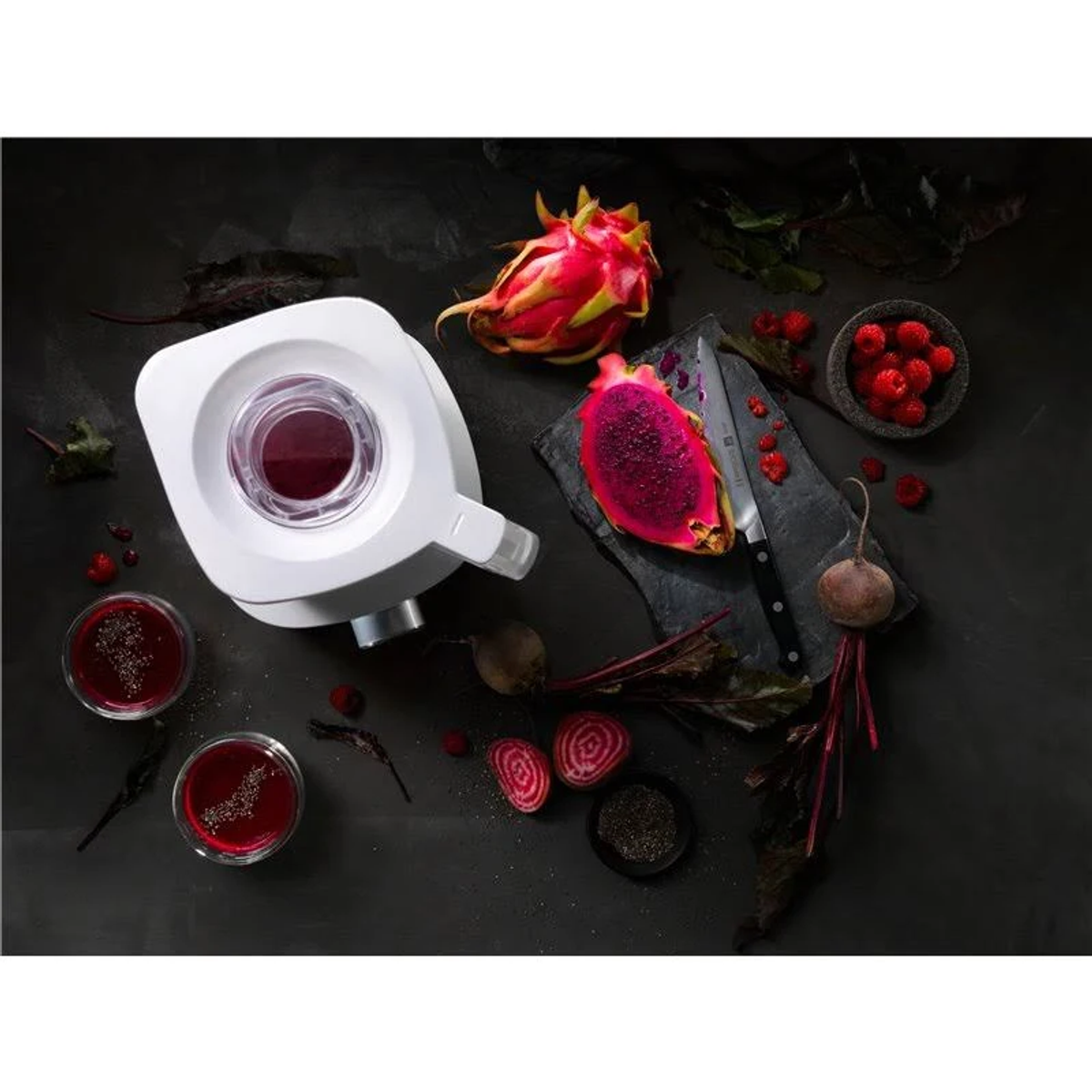 Wyiskarki do soku z smoczym owocem, burakami i nożem na ciemnej powierzchni.