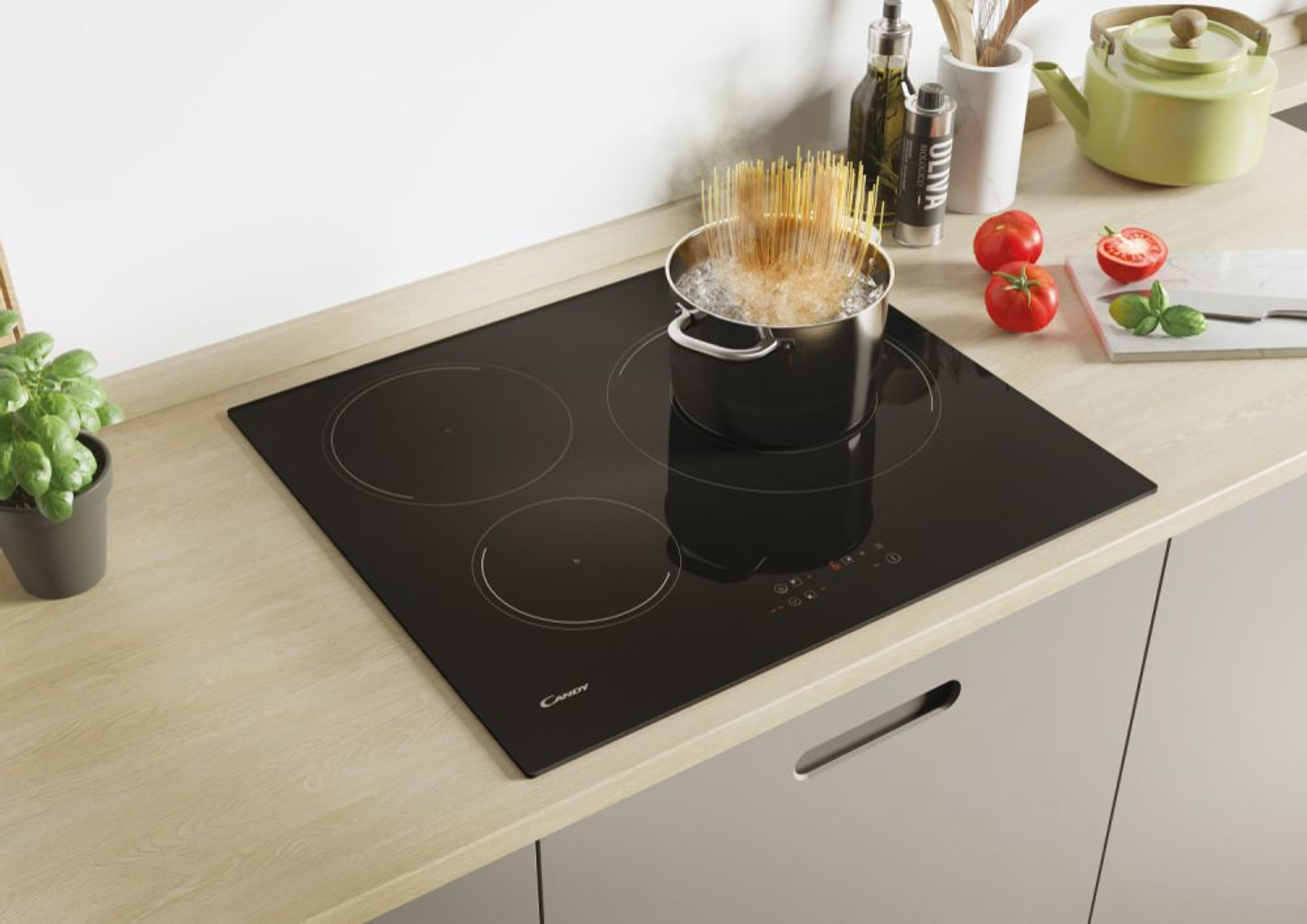 Una placa de inducción negra con una olla con agua hirviendo, pasta y tomates.