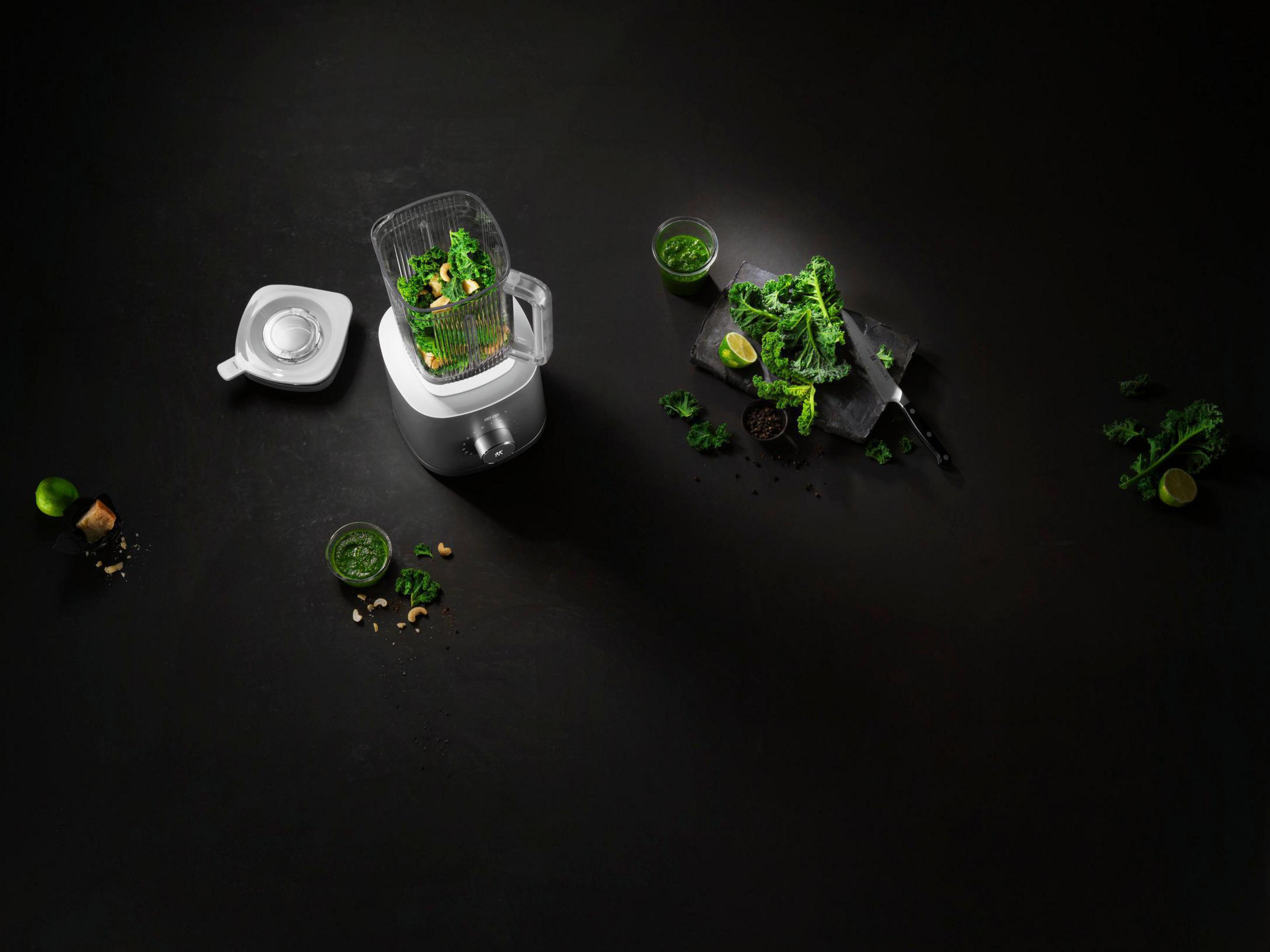 Blender z jarmużem w środku, inne składniki. Jarmuż, pesto i inne produkty spożywcze na czarnej powierzchni.