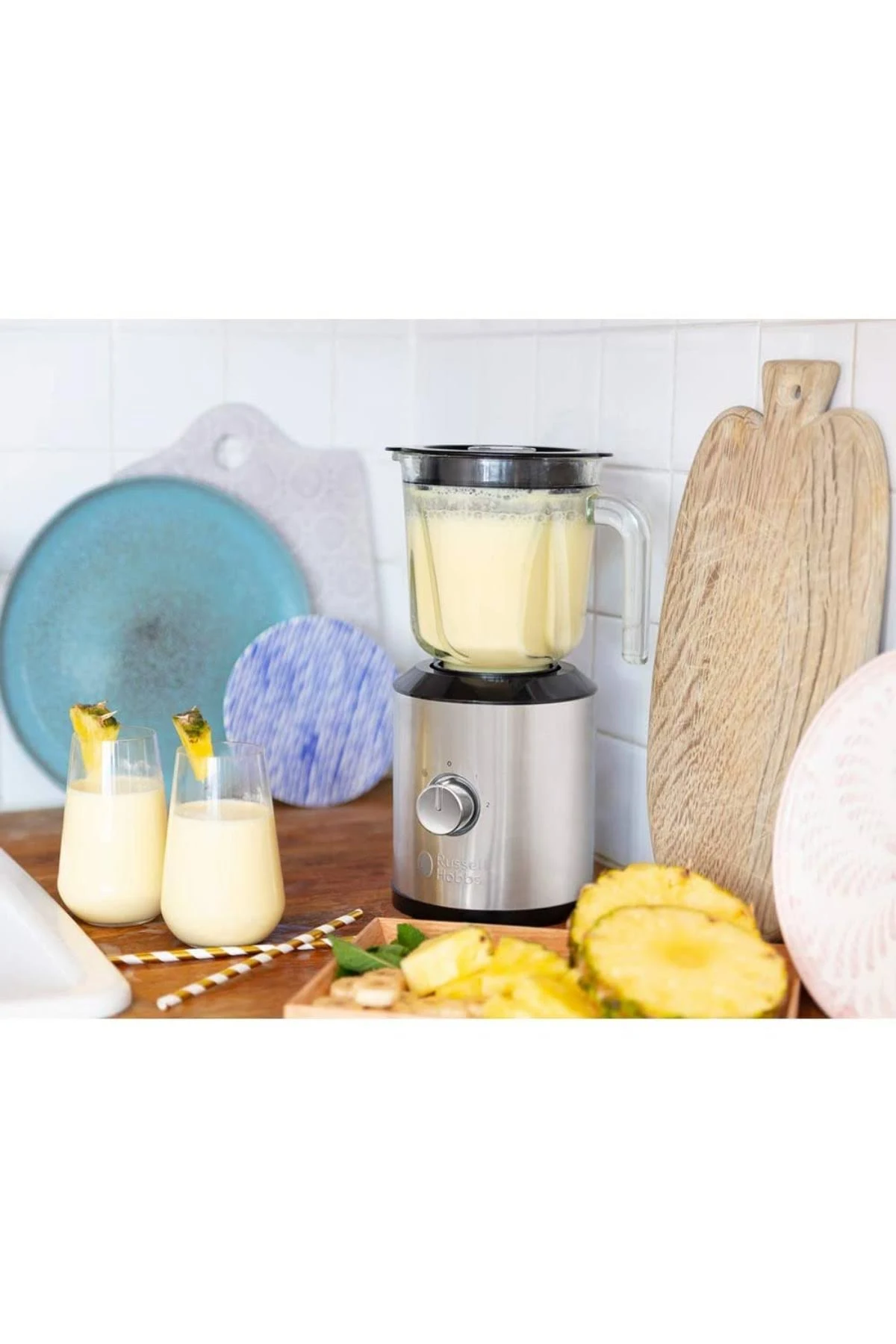 İçinde sarı sıvı olan bir blender, iki bardak sarı içecek ve ahşap bir tahtada ananas dilimleri.
