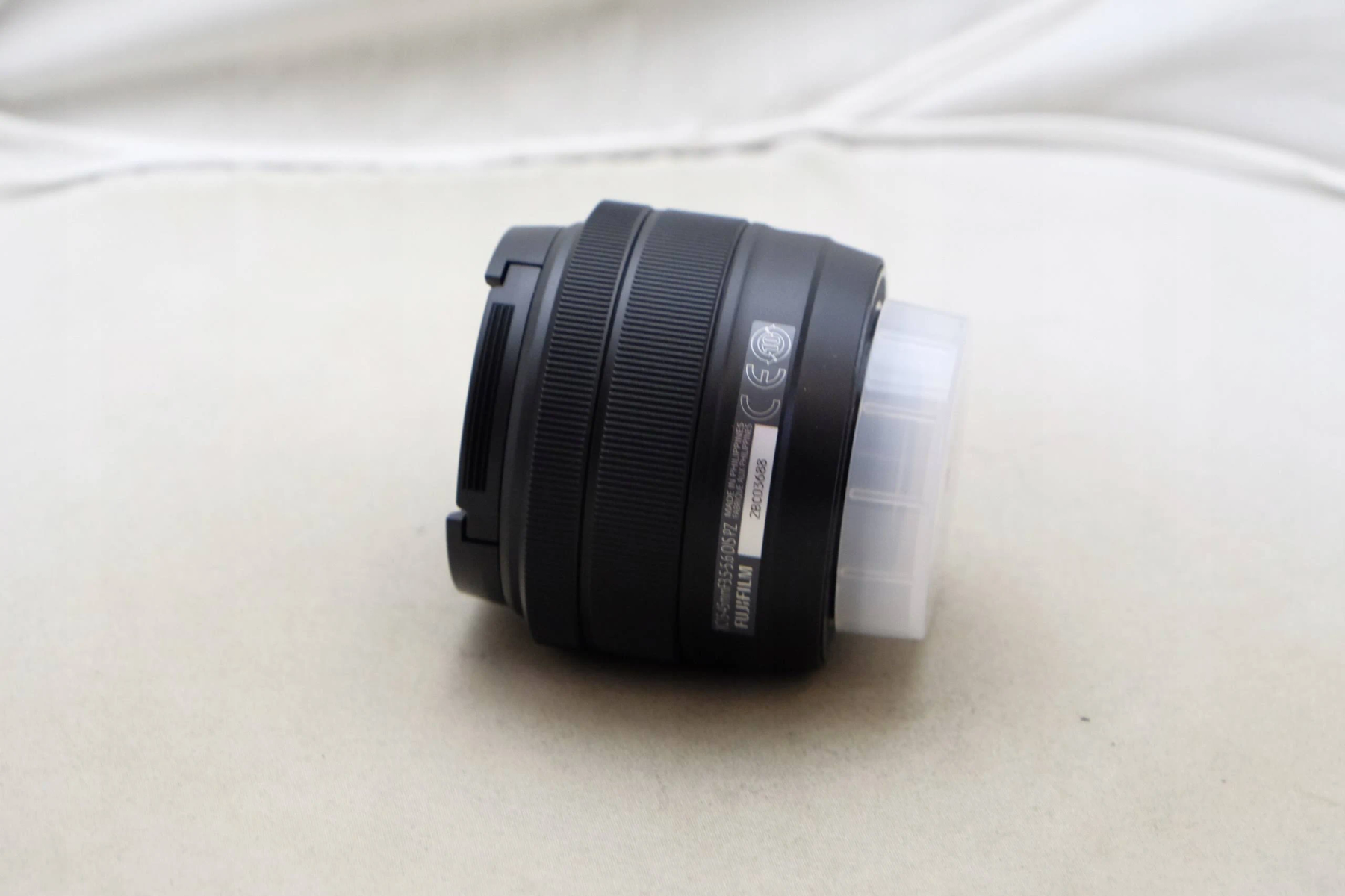 Czarny obiektyw aparatu na białej powierzchni. Obiektyw jest lekko pochylony.