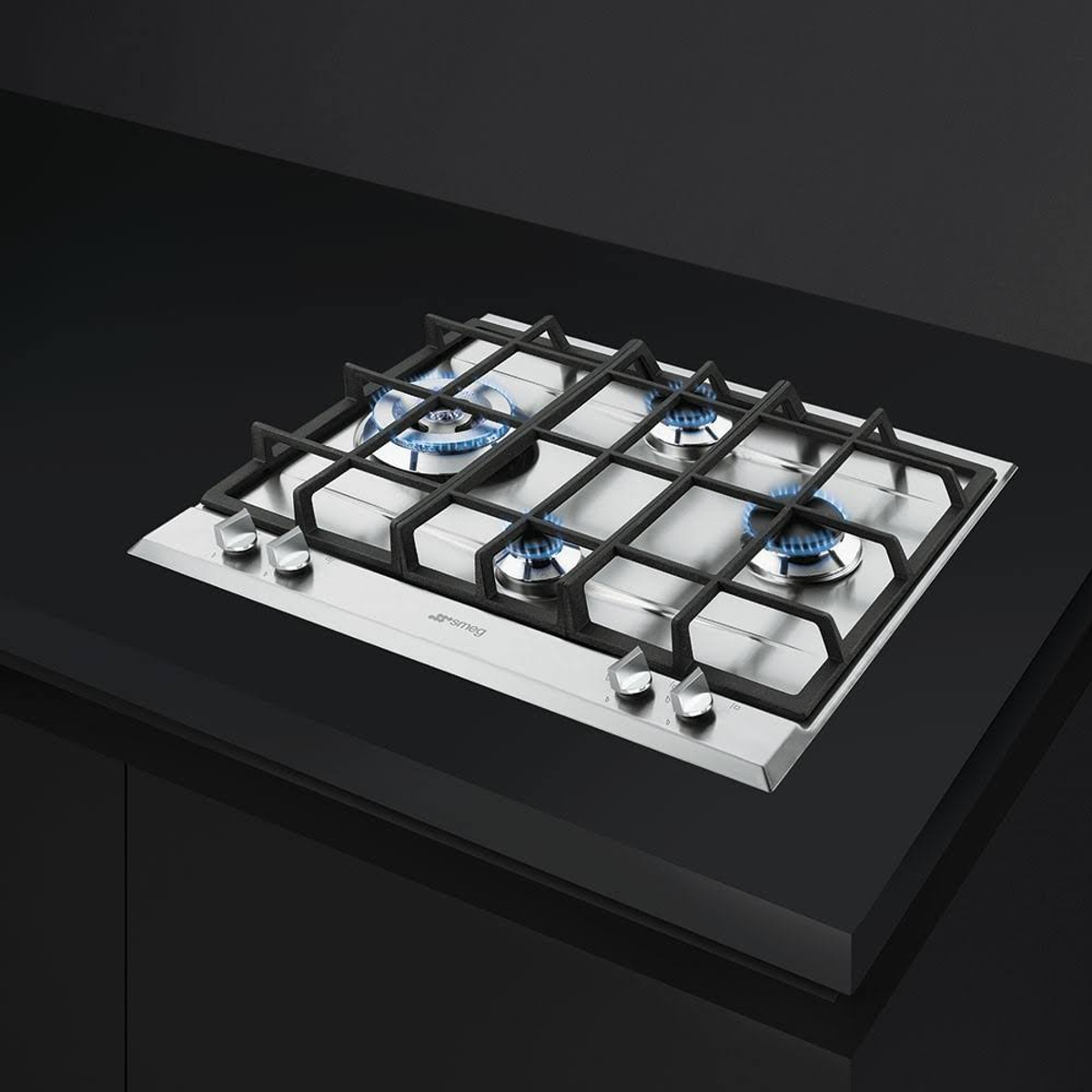 Stalowa płyta gazowa na czarnej powierzchni. Cztery palniki z niebieskimi płomieniami.