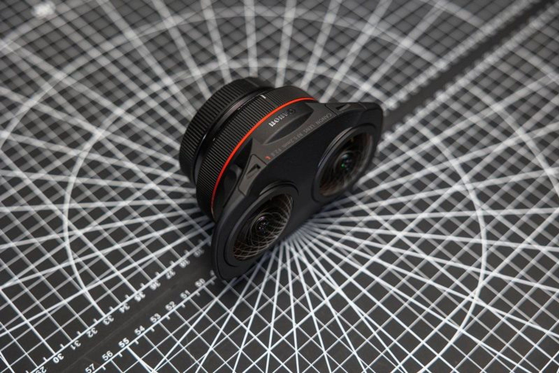 Un obiettivo nero con anello rosso e segni, su una griglia. Ha due lenti e un'etichetta Canon.