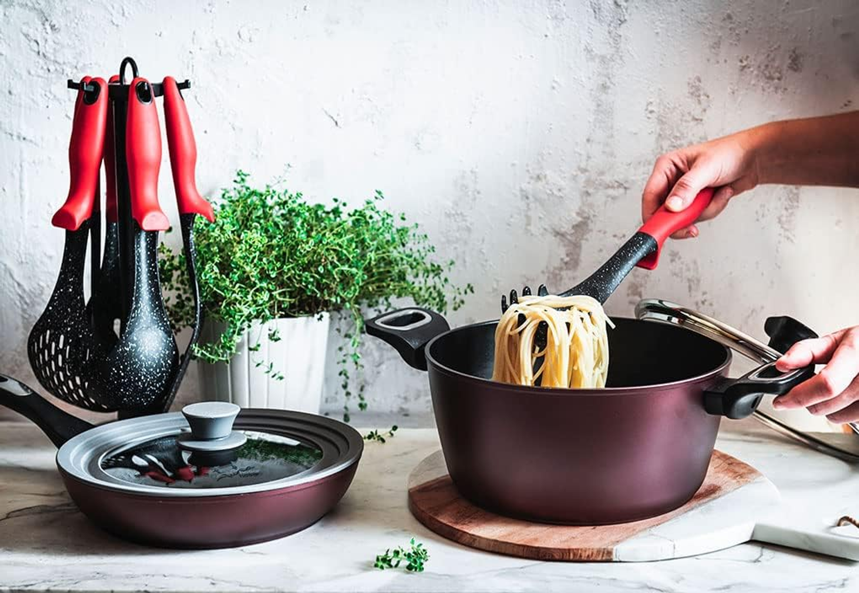 Frau kocht Pasta. Rotgriff Werkzeuge in einem Topf. Weitere Töpfe und Pflanzen im Hintergrund.