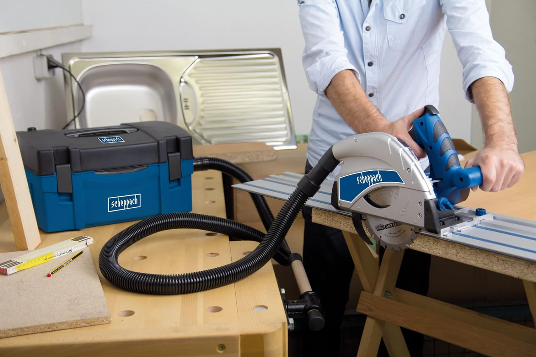 Mężczyzna używający piły tarczowej do cięcia drewna, z podłączonym odkurzaczem. Scena warsztatowa.