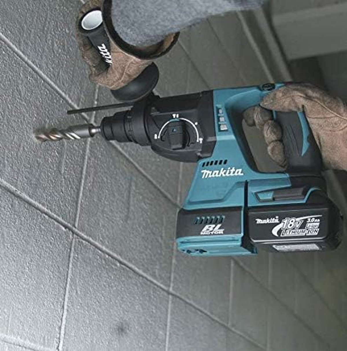 Una persona che fora un muro di mattoni grigi con un trapano Makita nero e verde acqua.
