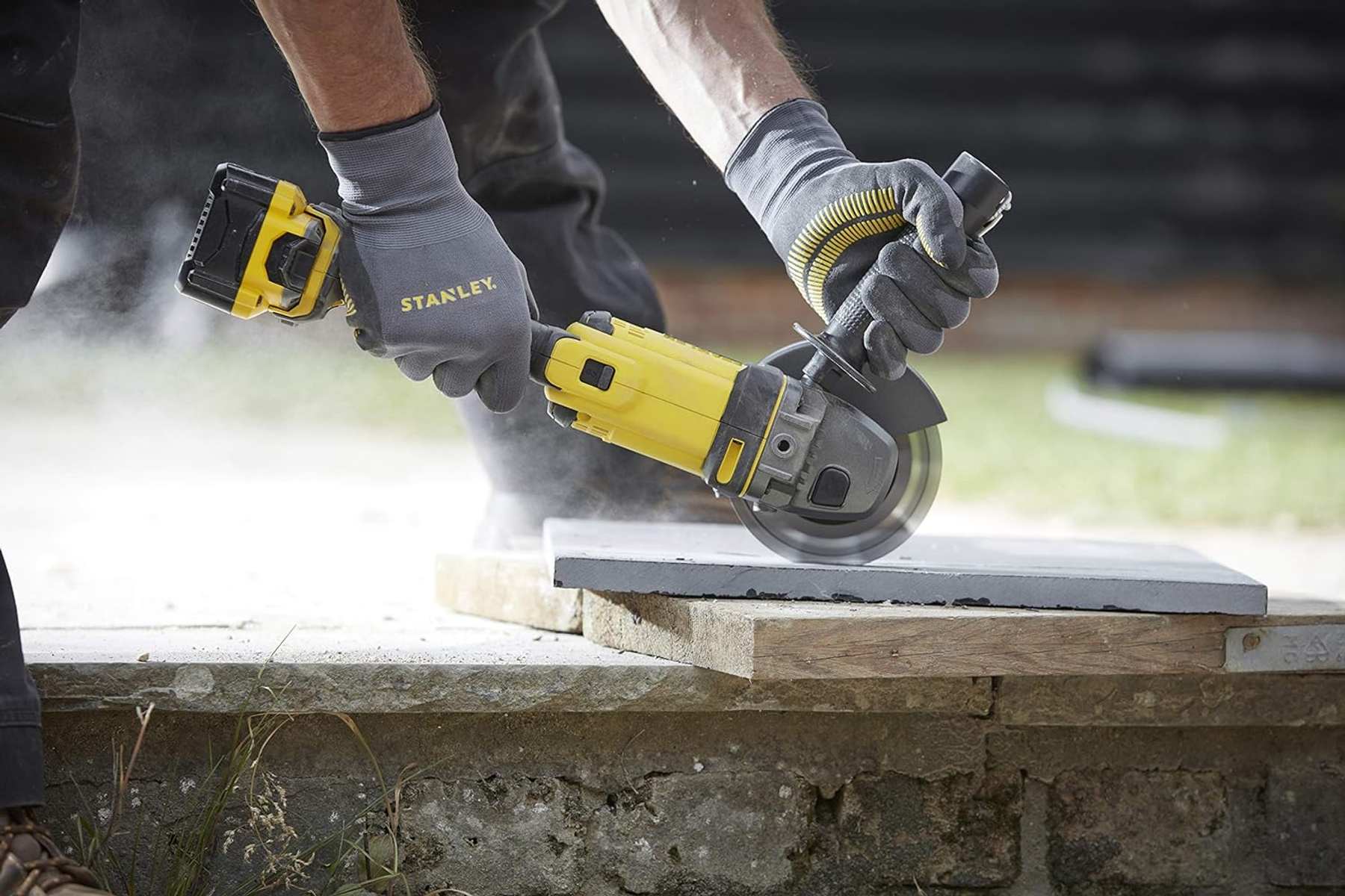 Robotnik używający żółto-czarnej szlifierki kątowej na kamiennej płycie, w rękawicach.