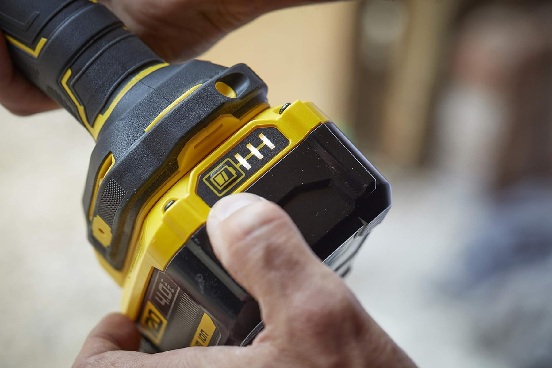 Ręce trzymają żółto-czarne elektronarzędzie ze wskaźnikiem baterii.