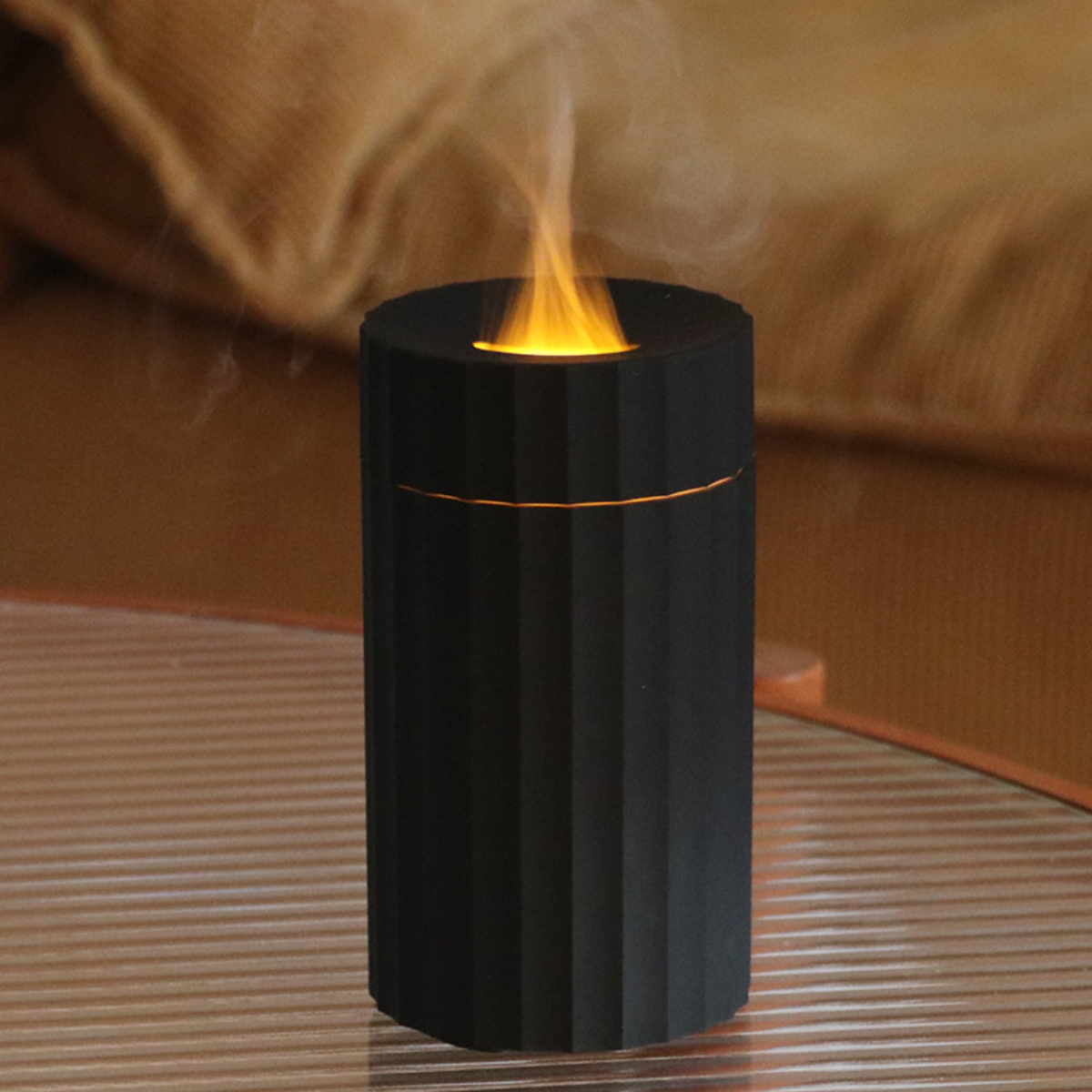 Ein schwarzer, zylindrischer Aromatherapie-Diffusor mit flammähnlichem Licht oben, der auf einem Tisch steht.