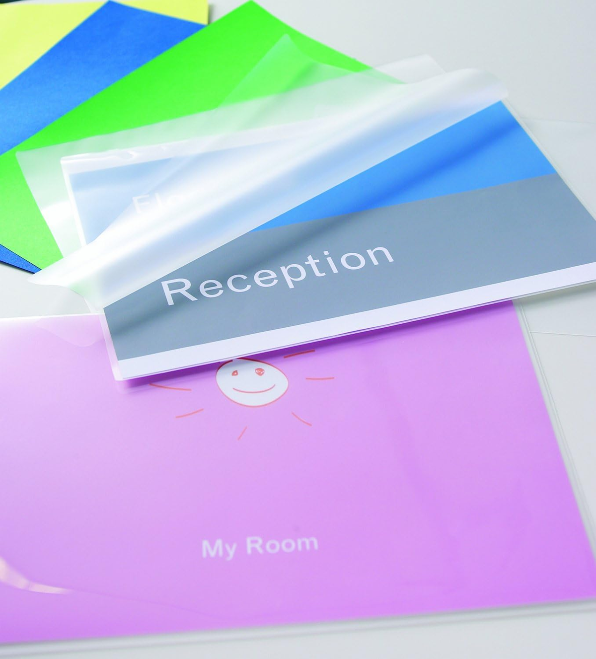 Ein Stapel bunter Dokumente mit einer transparenten Kunststofffolie obenauf, mit dem Wort 'Rezeption'.