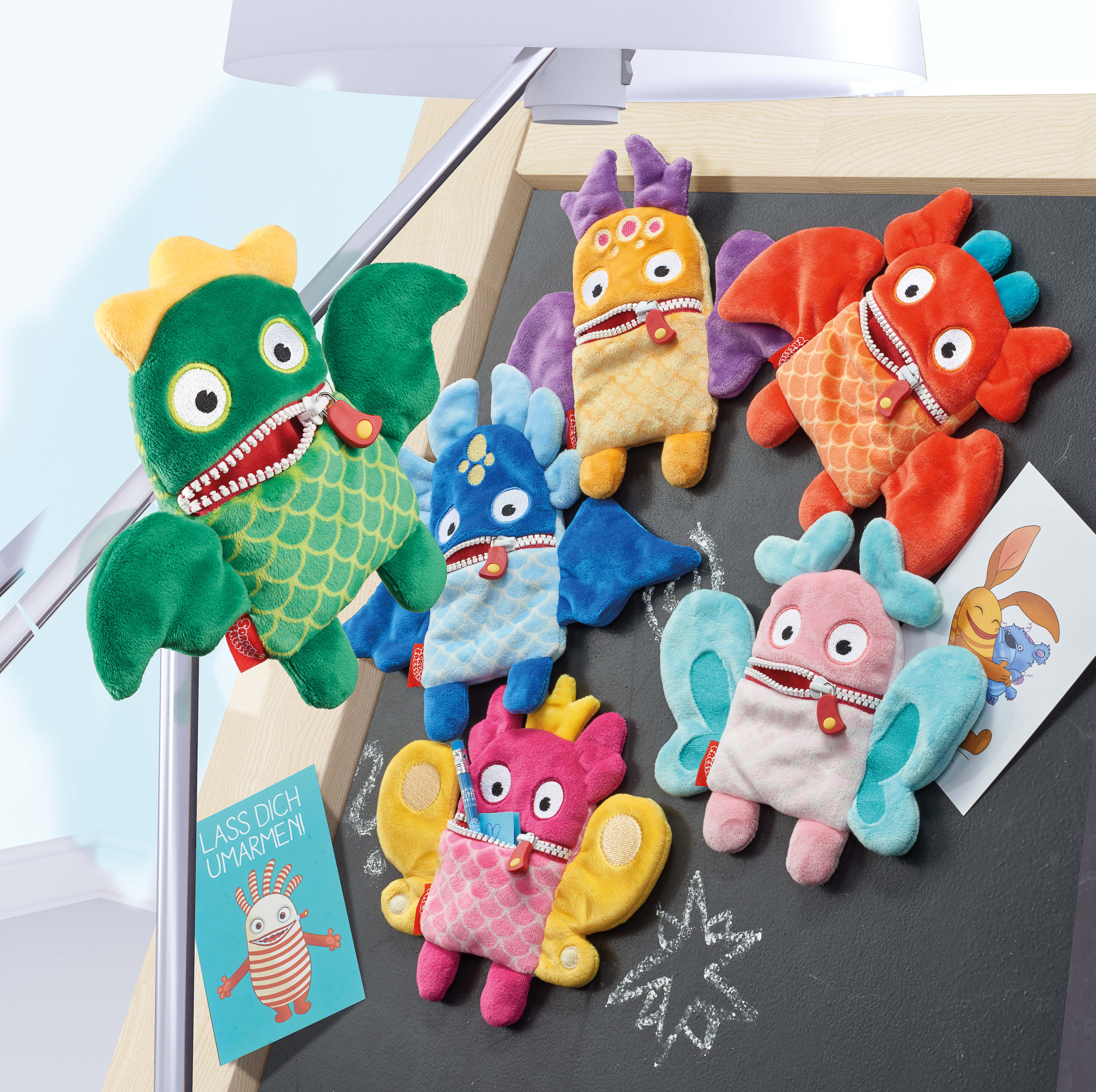 Bunte Plüschmonster in der Nähe einer Tafel. Verschiedene Formen und Farben.