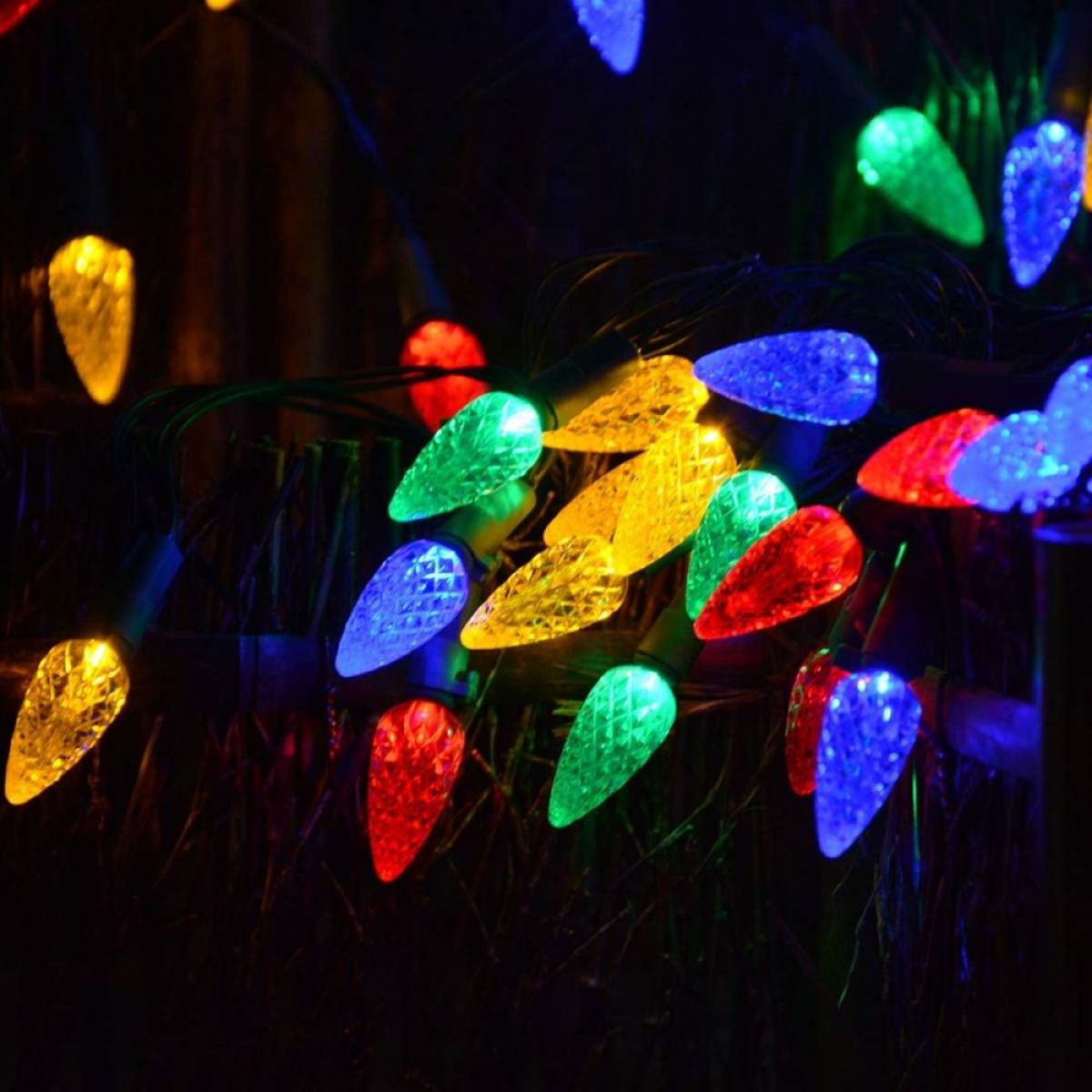 Nahaufnahme von bunten Weihnachtslichtern, jede wie ein Tannenzapfen geformt, vor dunklem Hintergrund.