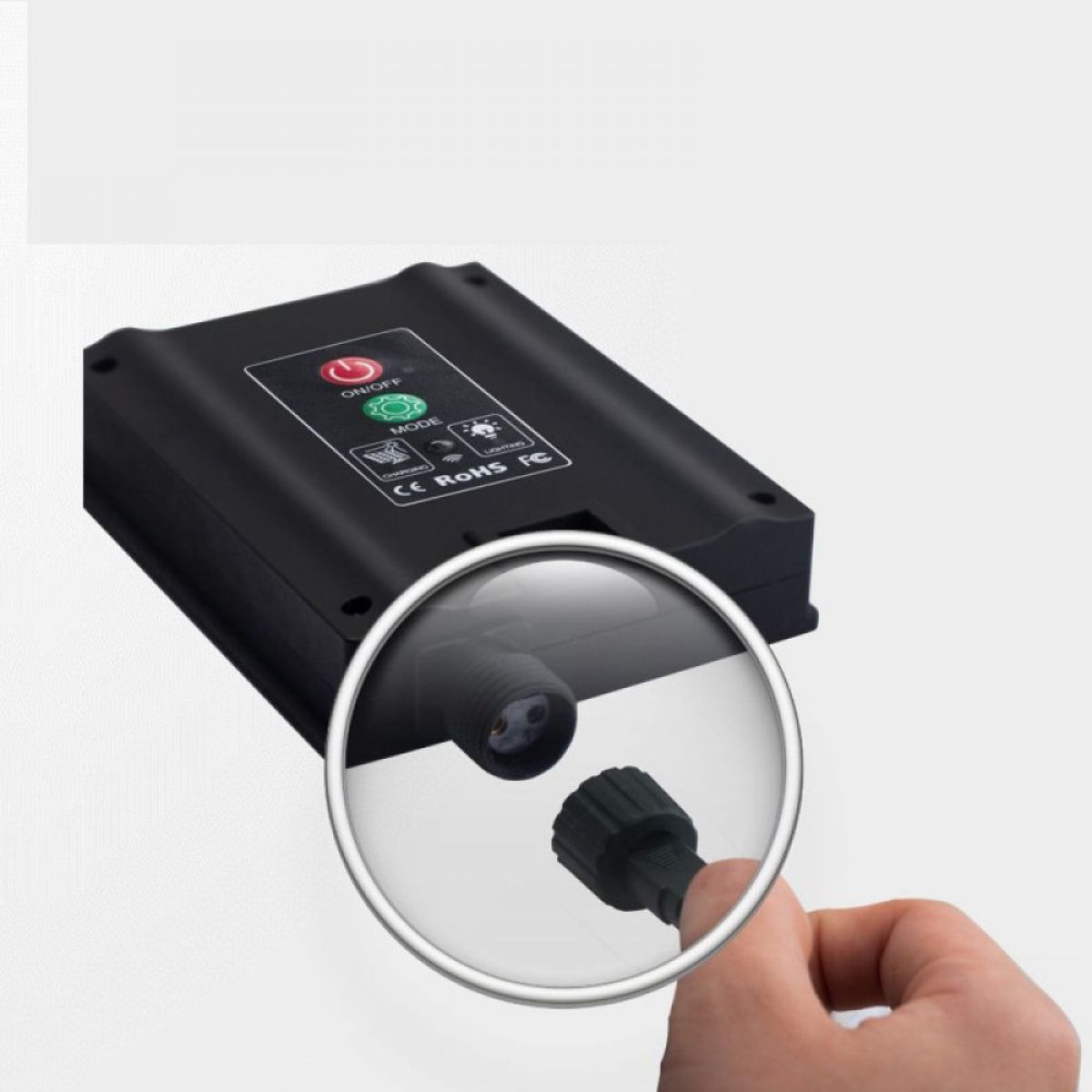Schwarzes elektronisches Gerät mit Knöpfen, Kabel und eine Person hält eine Lupe.