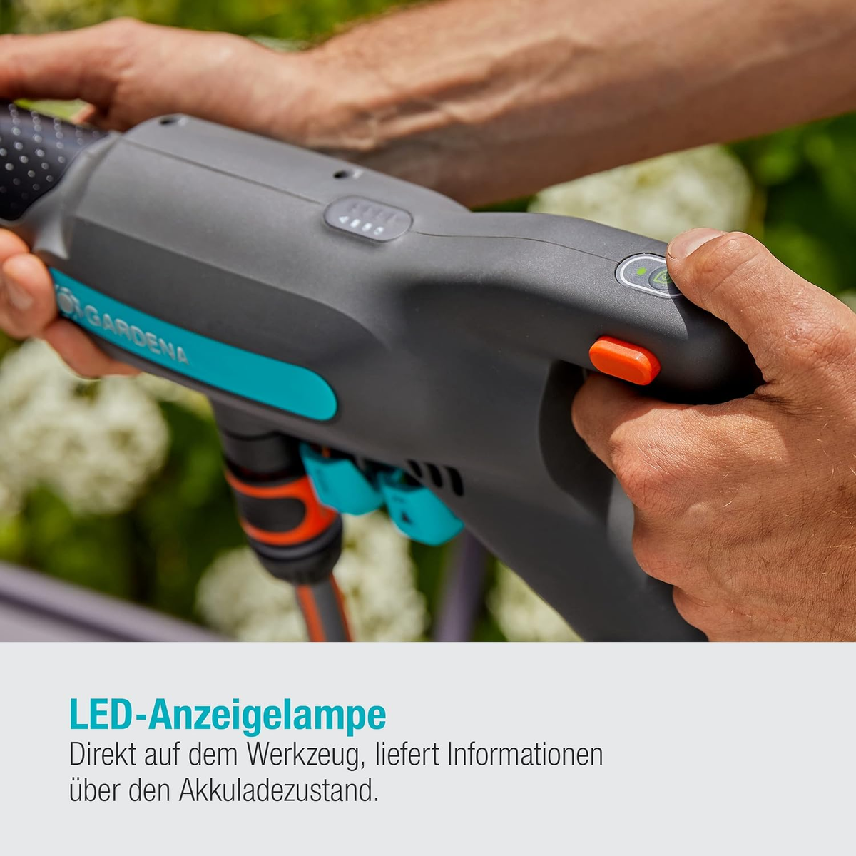 Hände einer Person halten ein graues Gartengerät mit einer orangefarbenen Taste und Kontrollleuchten.
