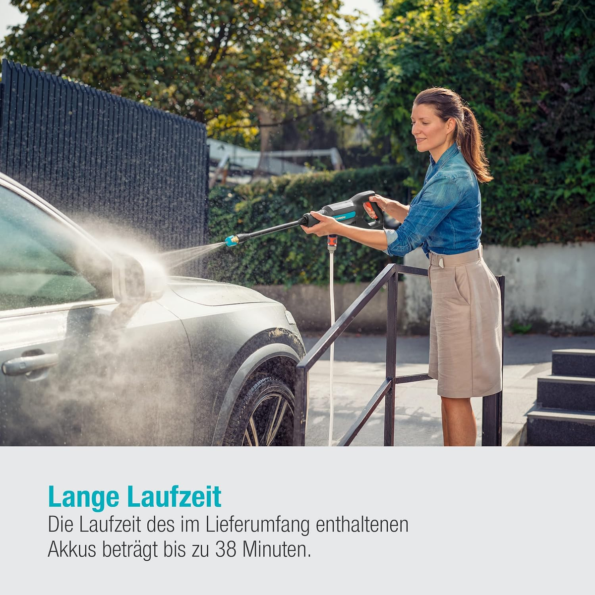Eine Frau wäscht ein silbernes Auto mit einem Hochdruckreiniger im Freien an einem sonnigen Tag.